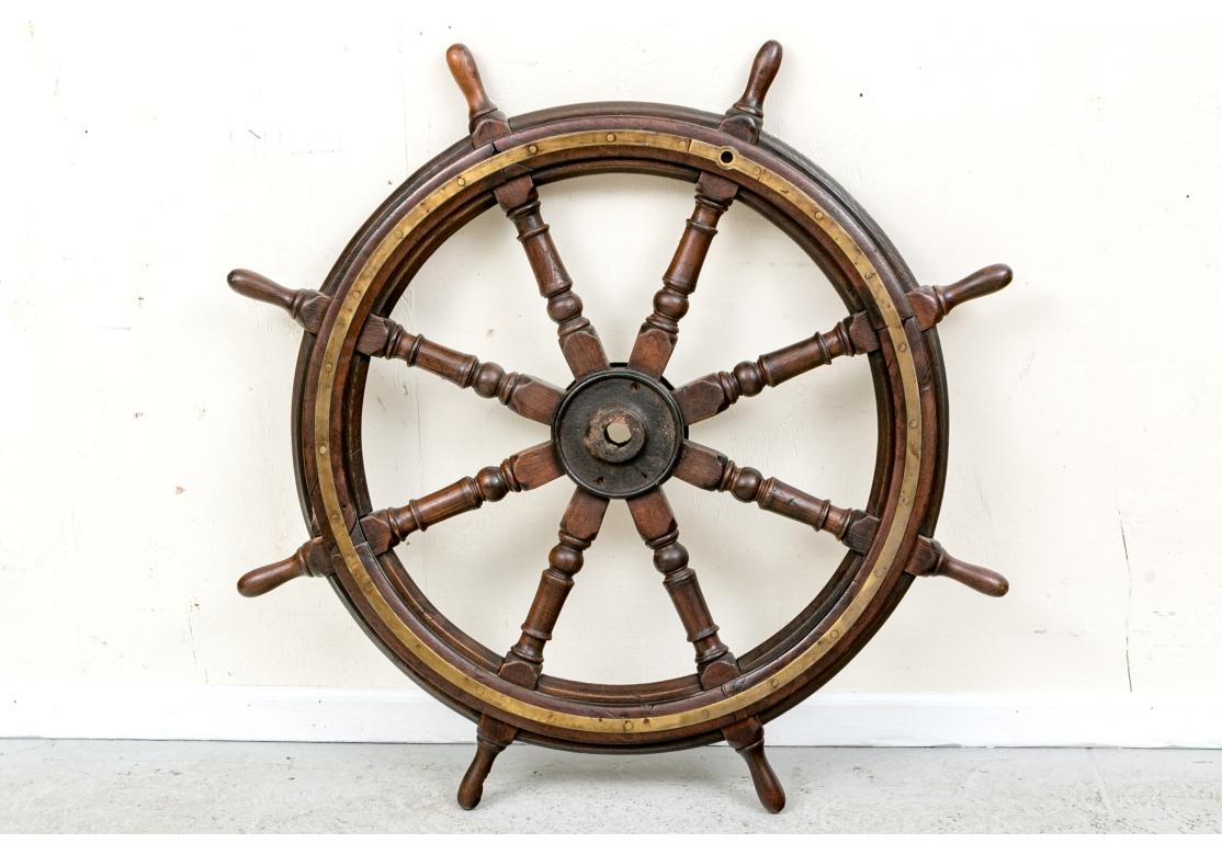 An antique solid mahogany Ship’s Wheel with 8 turned spokes having good size and weight. The axle has an iron core and polished brass front cap on one side. Both sides of the wheel have handsome brass banding.

Dimensions: 44 1/2