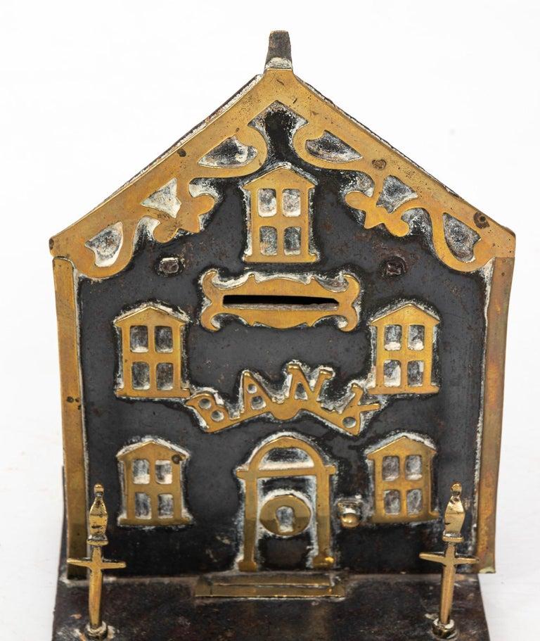 Save your pennies in this charming antique coin bank in the shape of a house. Made from brass with gilded architectural details. Sourced from England, it was made in the early 20th century. A nice collectible piece, it retains its original patina