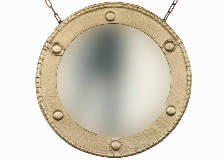 Late 19th century Federal styled round wall mirror featuring a hand-hammered solid brass surround with hand-hammered brass applied decorations with the original beveled mirror and brass chain. Mounted on wood.