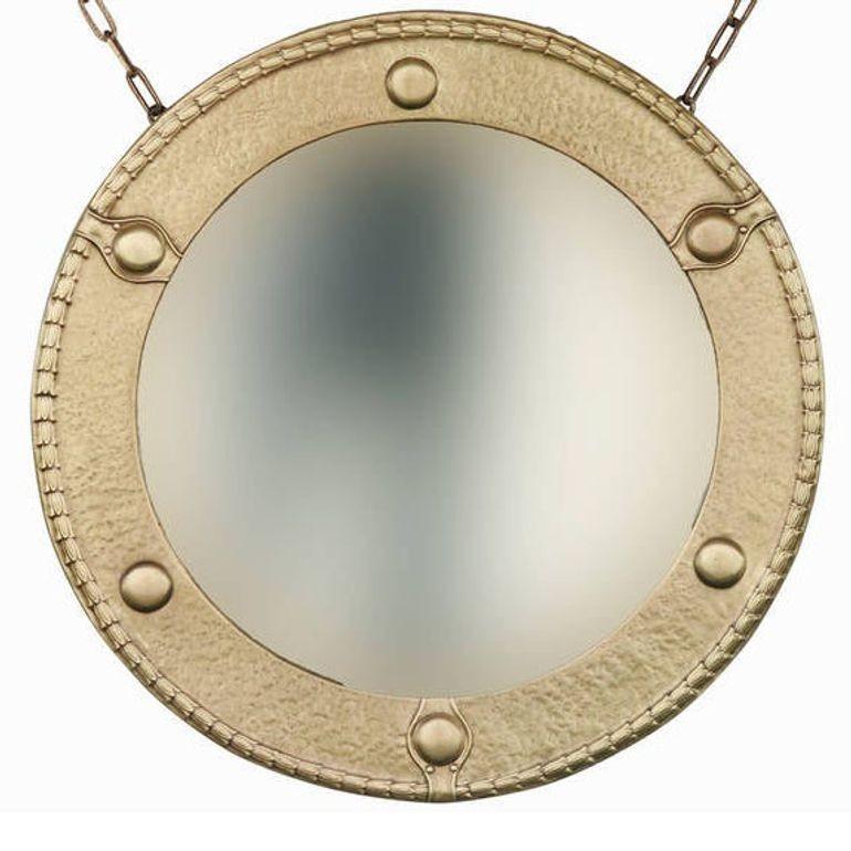 Late 19th century Federal styled round wall mirror featuring a hand-hammered solid brass surround with hand-hammered brass applied decorations with the original beveled mirror and brass chain. Mounted on wood.