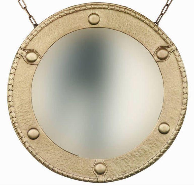Miroir mural rond de style fédéral de la fin du XIXe siècle, avec un entourage en laiton massif martelé à la main et des décorations appliquées en laiton martelé à la main, avec le miroir biseauté d'origine et une chaîne en laiton. Monté sur bois.