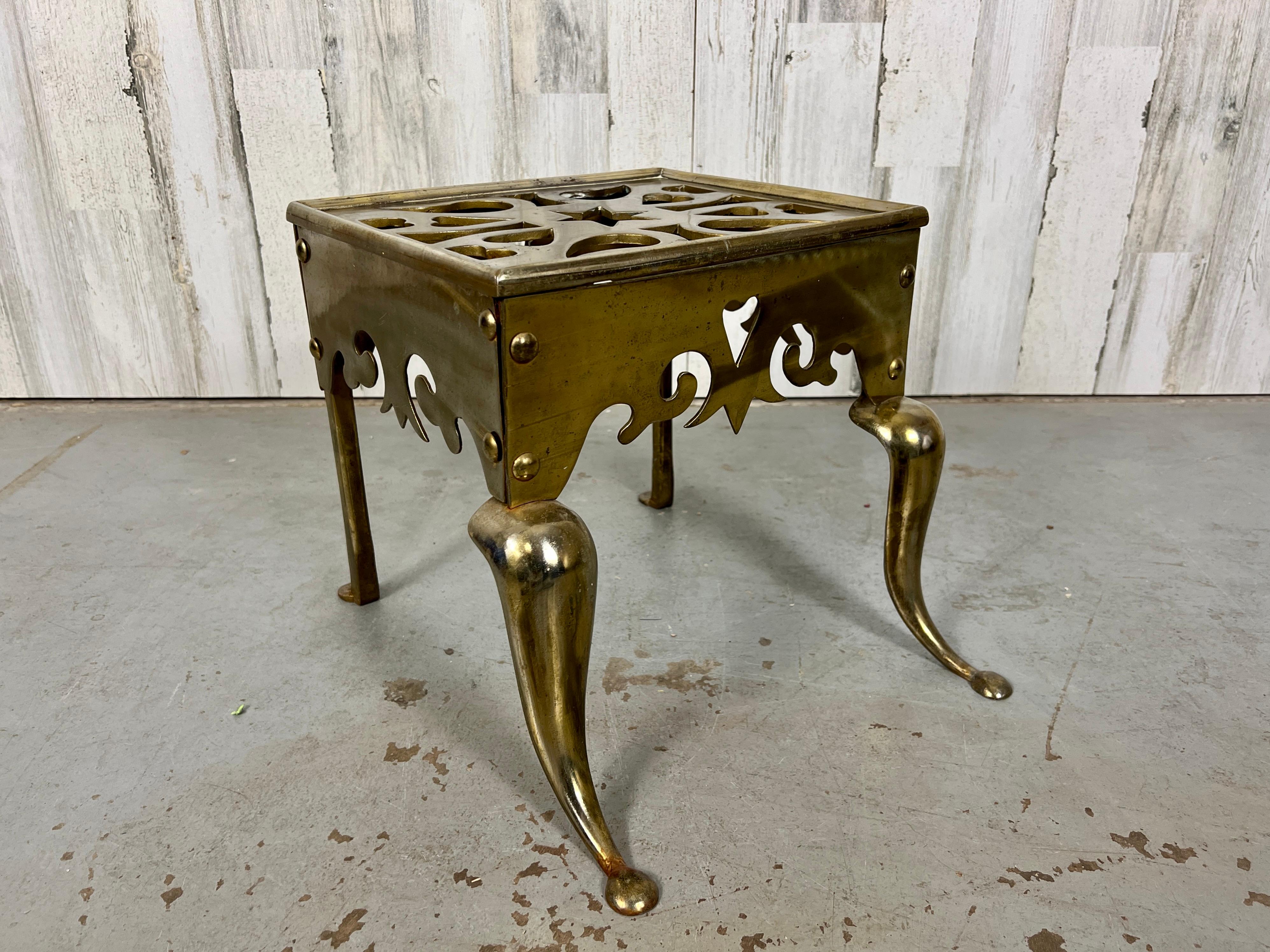 A remarkable fireplace trivet or footman stool crafted in the early 19th century from brass-plated steel. This piece is ideal for serving as a bench or stand, showcasing cabriole front legs and an intricate leaf pattern design on the top.