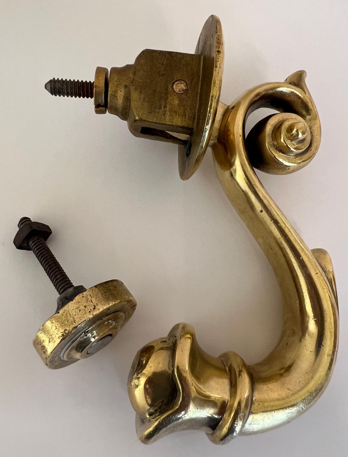 Antique brass French door knocker in a French flourish and swirl at the top. The backplate paired is round with an iron screw.