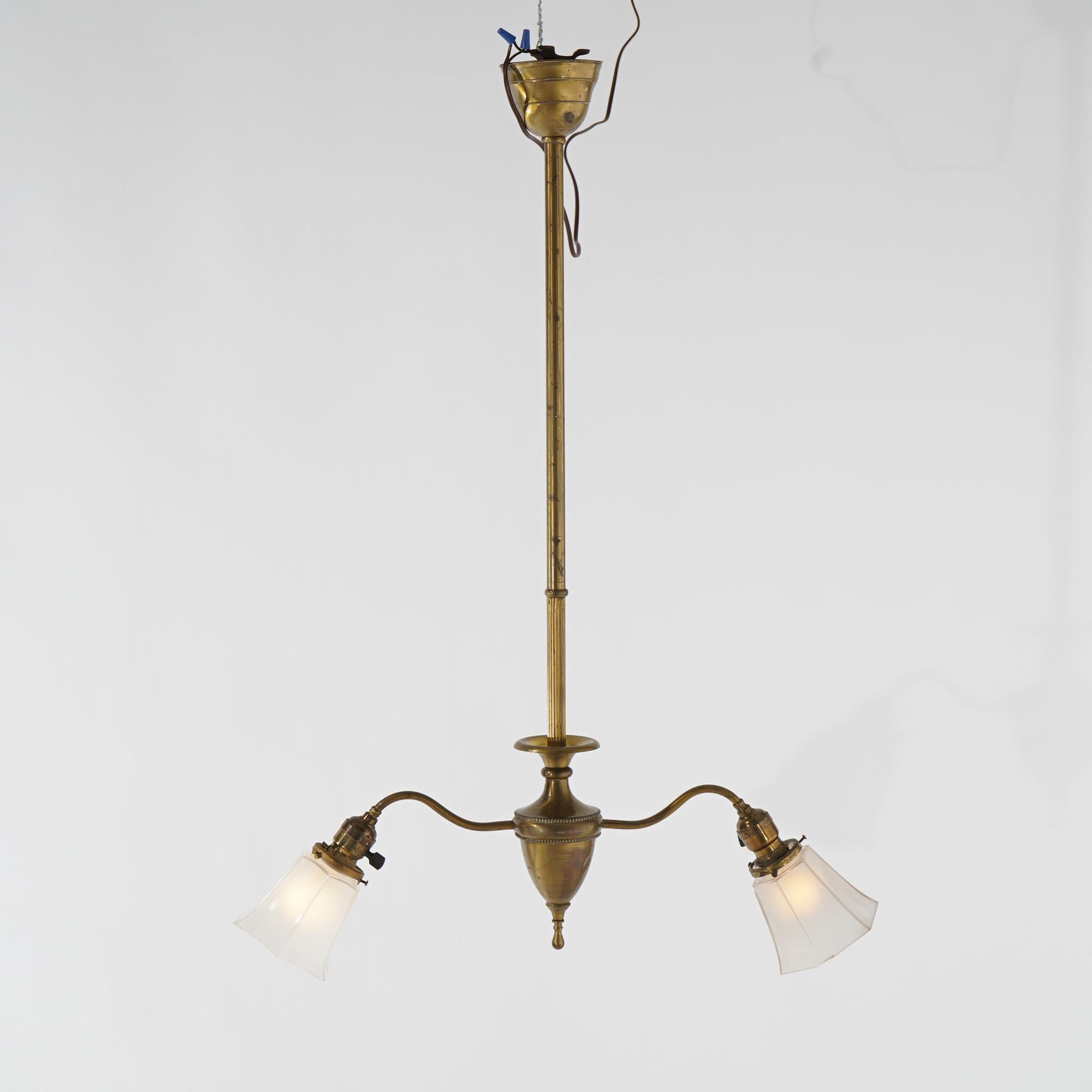An antique chandelier offers brass and gilt metal construction with urn form font having two scroll arms terminating in lights having glass shades, c1920

Measures - 36