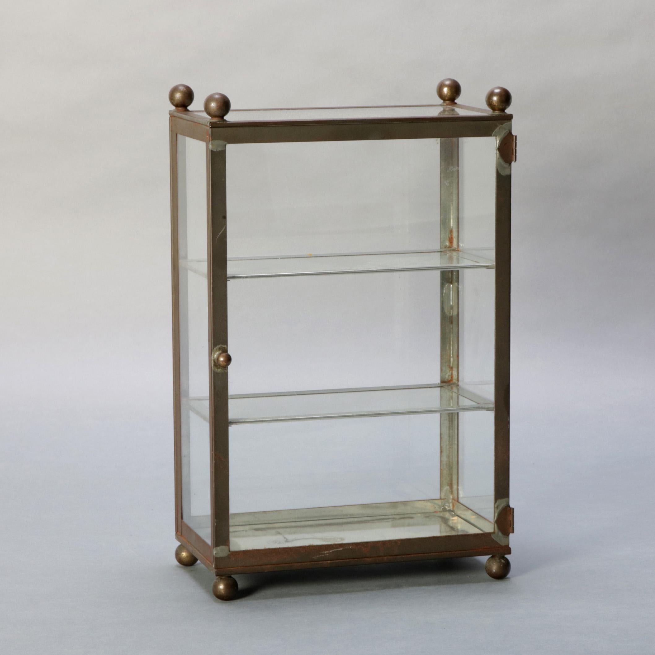 An antique dresser or counter top trinket or jewelry vitrine features brass frame with ball finials and feet with glass sides and door opening to display having two glass shelves and mirrored base, 20th century

Measures: 16.25