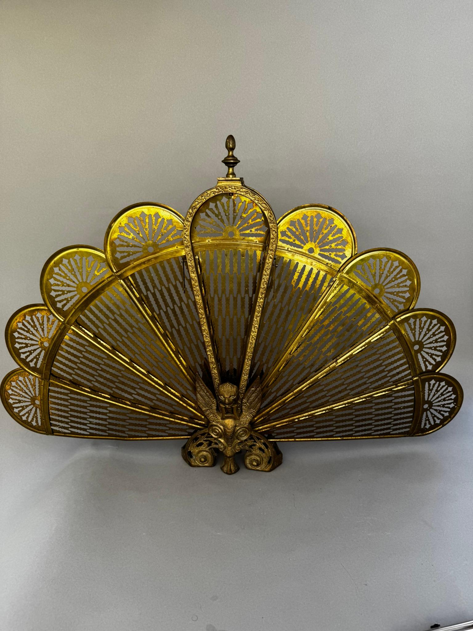 Este exquisito guardafuegos antiguo data de principios del siglo XX y presenta un icónico diseño de abanico de pavo real, emparejado con una audaz figura central de grifo en su base. Fabricadas en latón macizo, las hojas plegables del biombo están