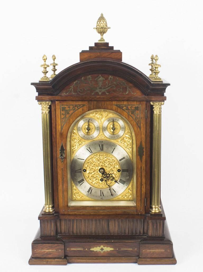 An impressive brass inlaid goncalo alves musical boardroom clock with triple fusee movement, late 19th century in date.

The gilded brass arched dial with decorative floral and foliate engraving. It has a 7 3/8 inch silvered chapter ring and