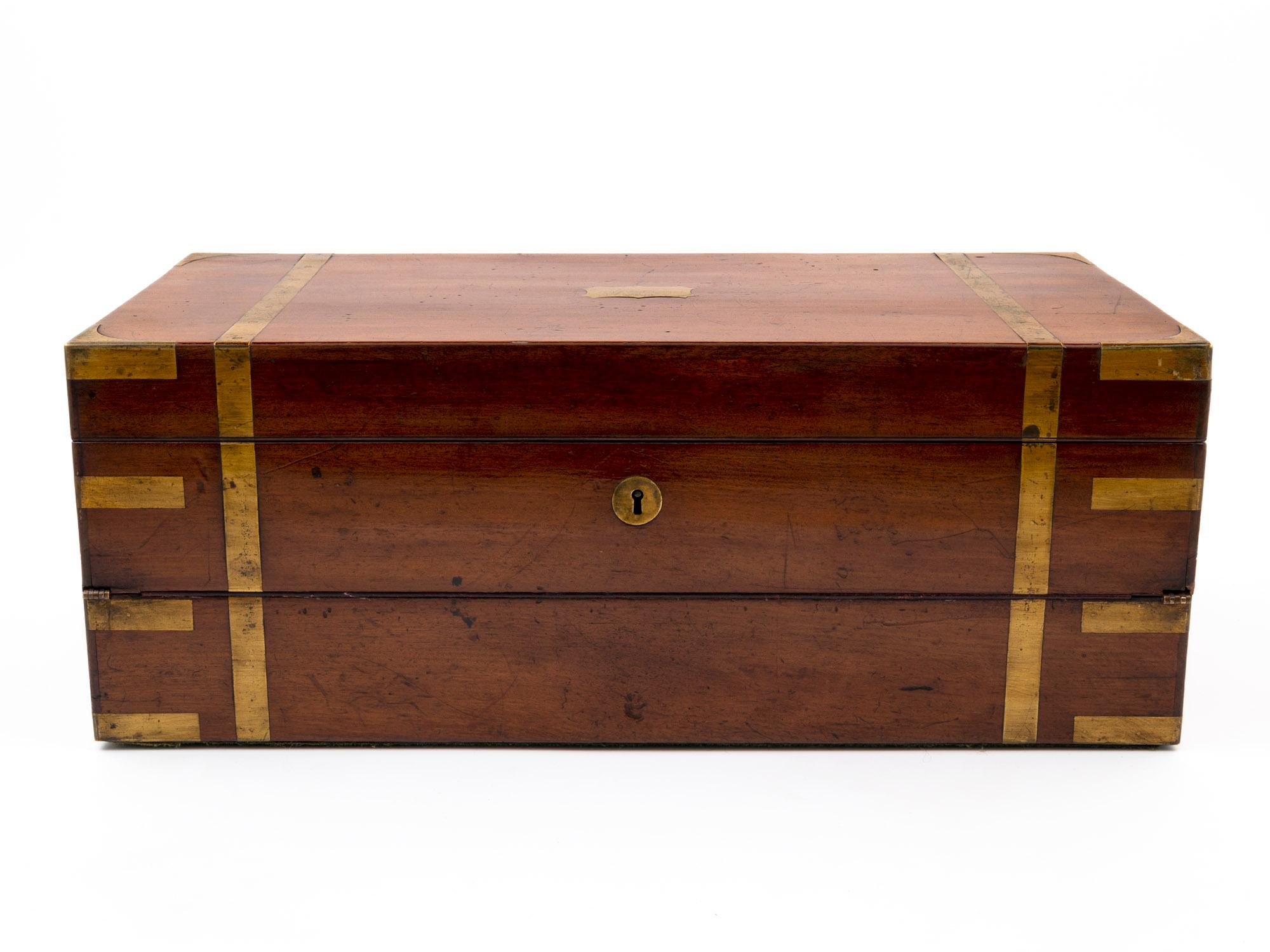 A large military-style solid Mahogany double opening writing box, with brass corner brackets, strapping and flush fitting campaign-style side handles. Contains a secret compartment with three hidden drawers. Lifting the lid reveals a maroon