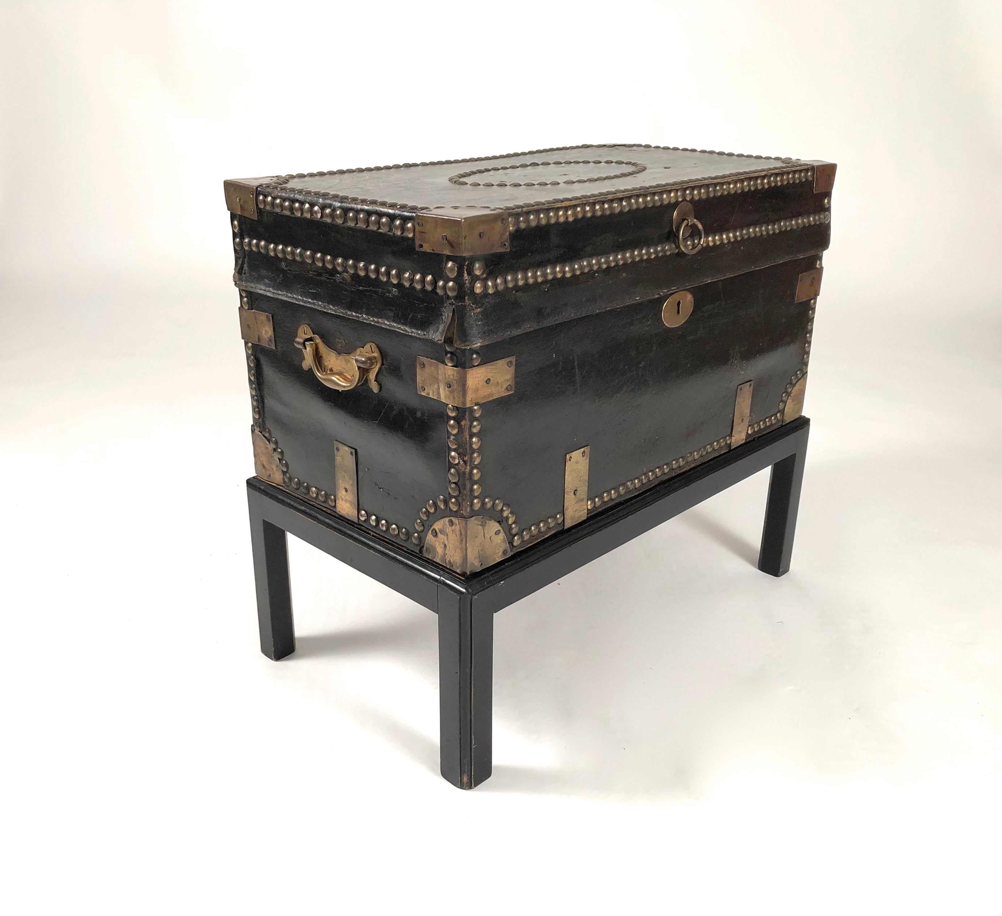 An antique brass stud decorated sea captain's chest on stand, circa 1810-1820, ideal as a side table. The interior is lined with its original coral colored printed wallpaper. The Stand was custom made for it and is black painted wood. Perfect as a