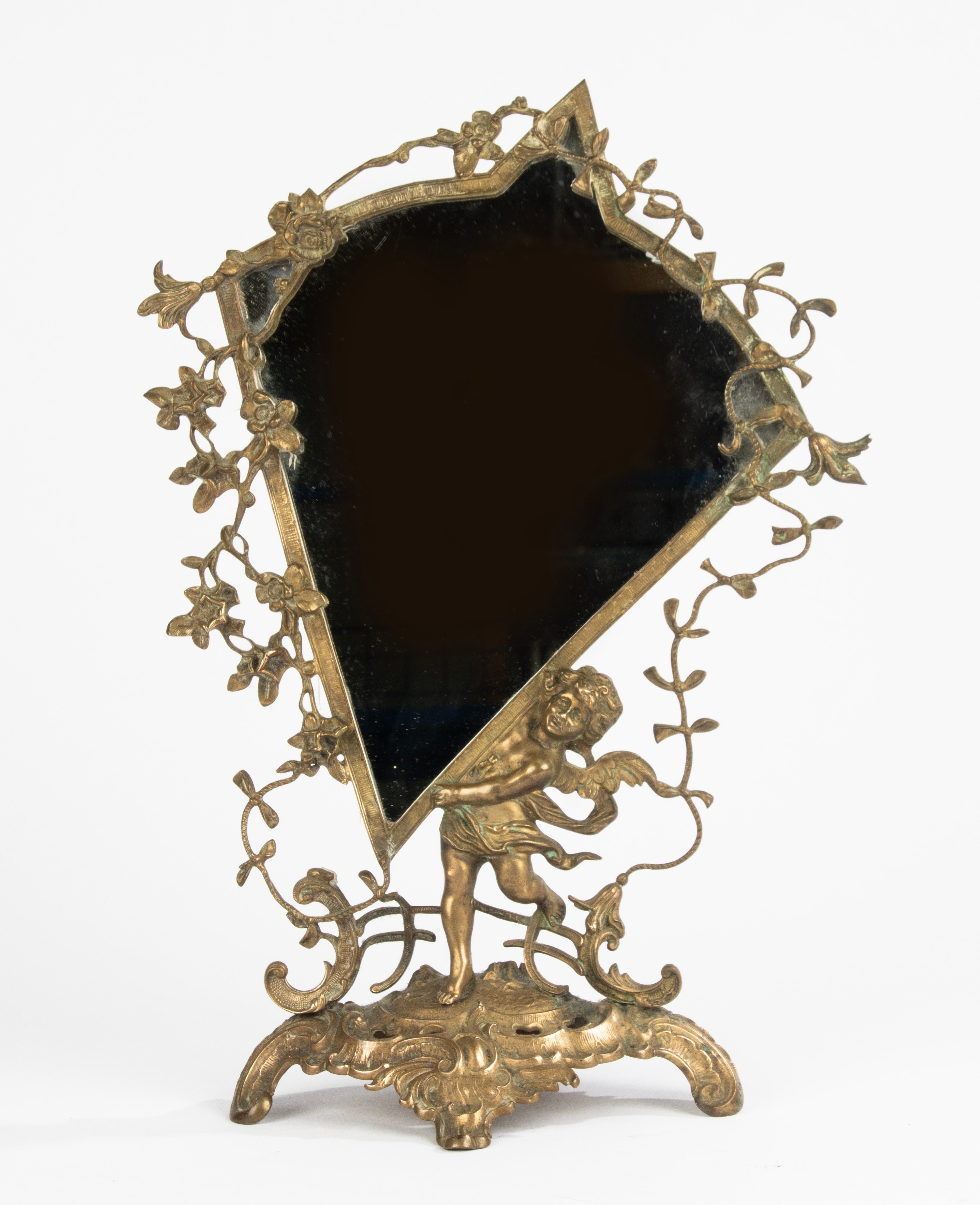 Un joli miroir de table en laiton. Forme spéciale, comme un cerf-volant, joliment décorée d'un angelot et de fleurs. 
La lampe est en bon état. Belle patine ancienne. 
Il semble que la vitre ait été remplacée récemment, le verre est également en bon