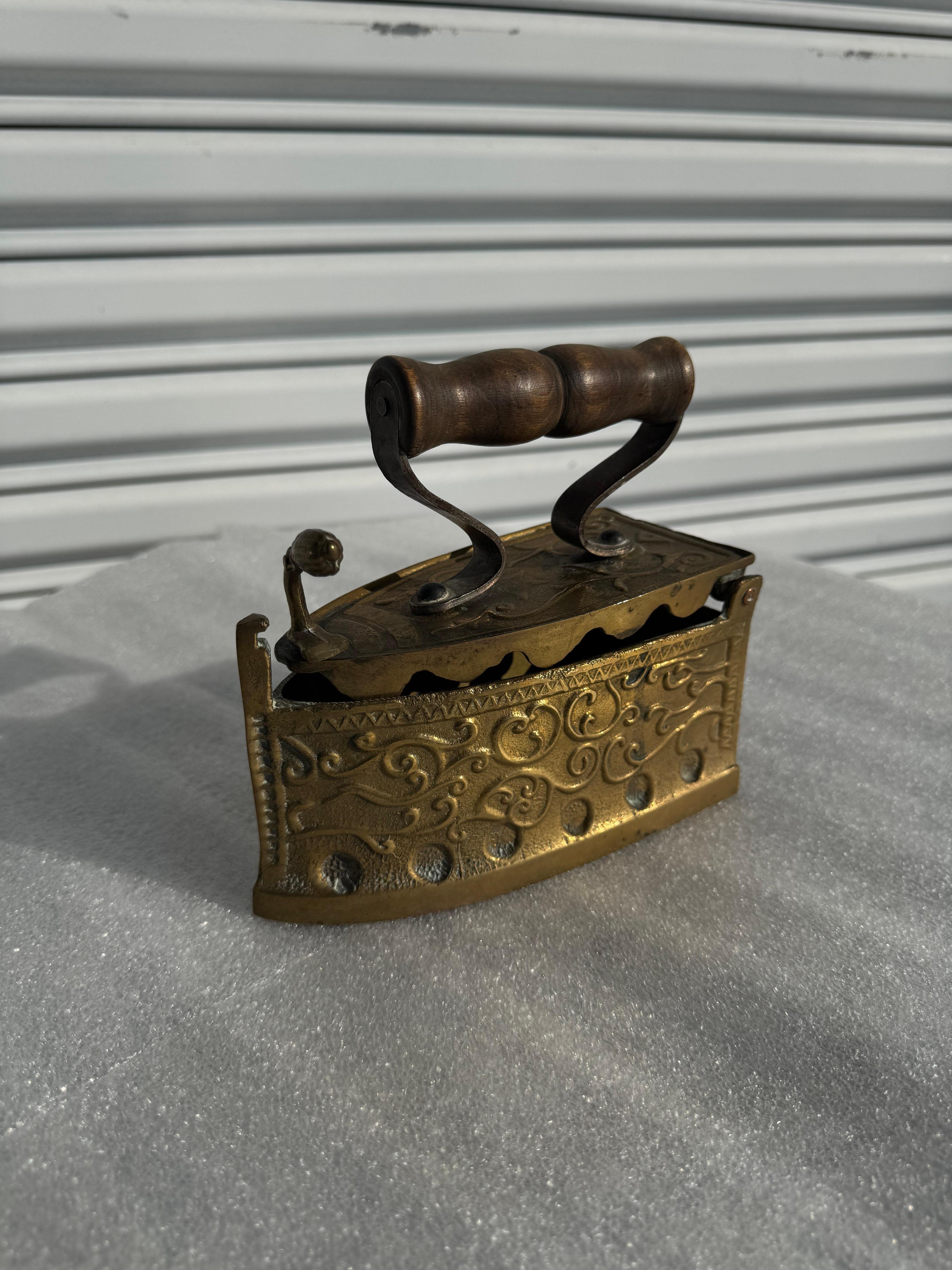 Si tratta di un ferro da stiro o ferro piatto che viene riscaldato con il carbone.
È realizzato in ottone fortemente inciso e ha un manico in legno.
La parte anteriore superiore ha una leva per sbloccare il ferro da stiro in modo da aprirlo e