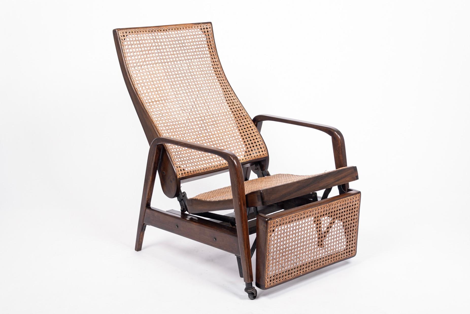 This unique antique Brazilian mechanical recliner lounge chair was made in the early 20th century. This exceptional chair is expertly handcrafted from solid walnut wood and features hand caned seat, backrest and footrest with metal caster wheels on