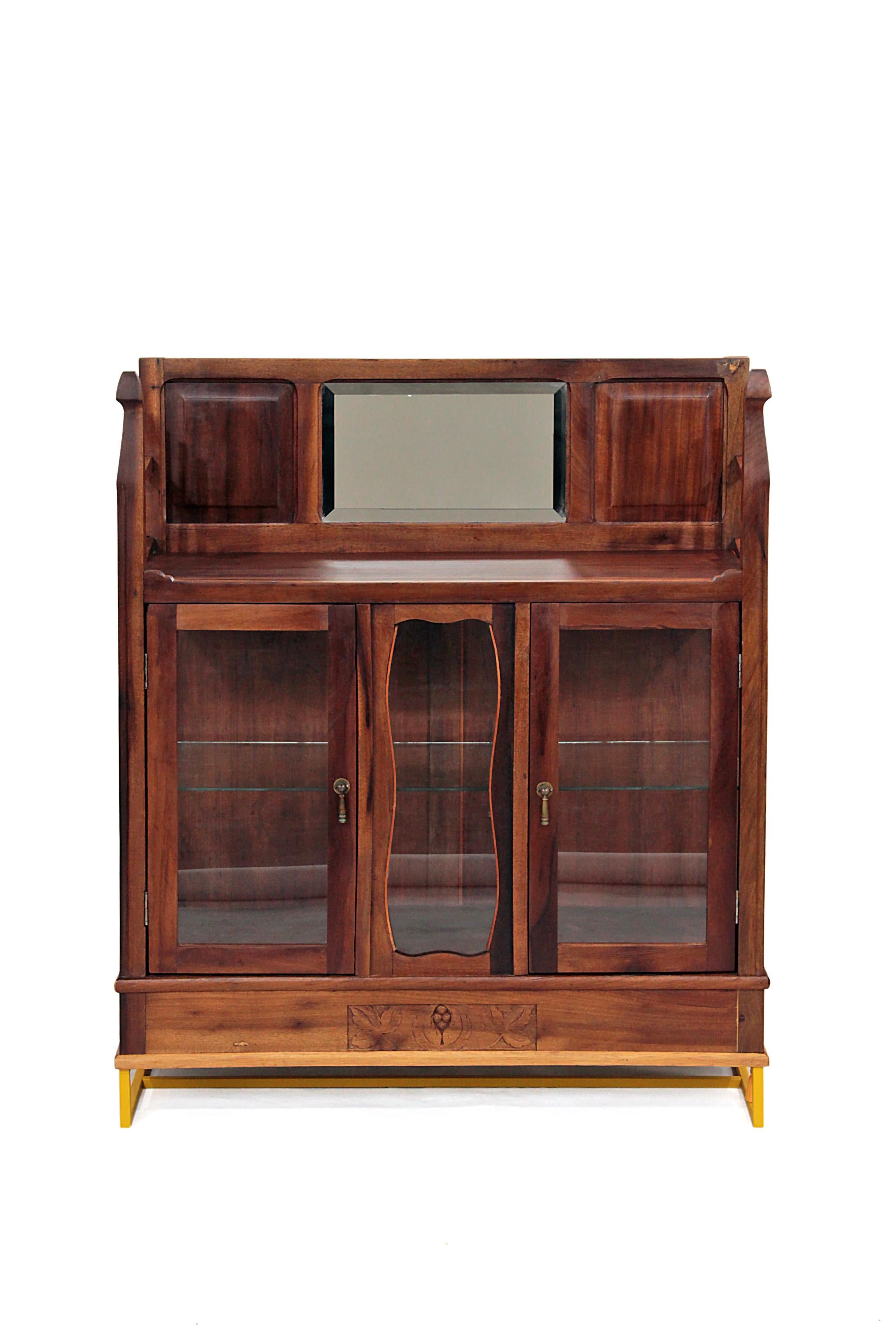 The glass cabinet - Restauro #1 (Restoration #1) is an antique Brazilian walnut cabinet restored with glass panels and shelf, antique looking brass handles and bright yellow steel base, in which are two 3D printed small statues. Since this a design