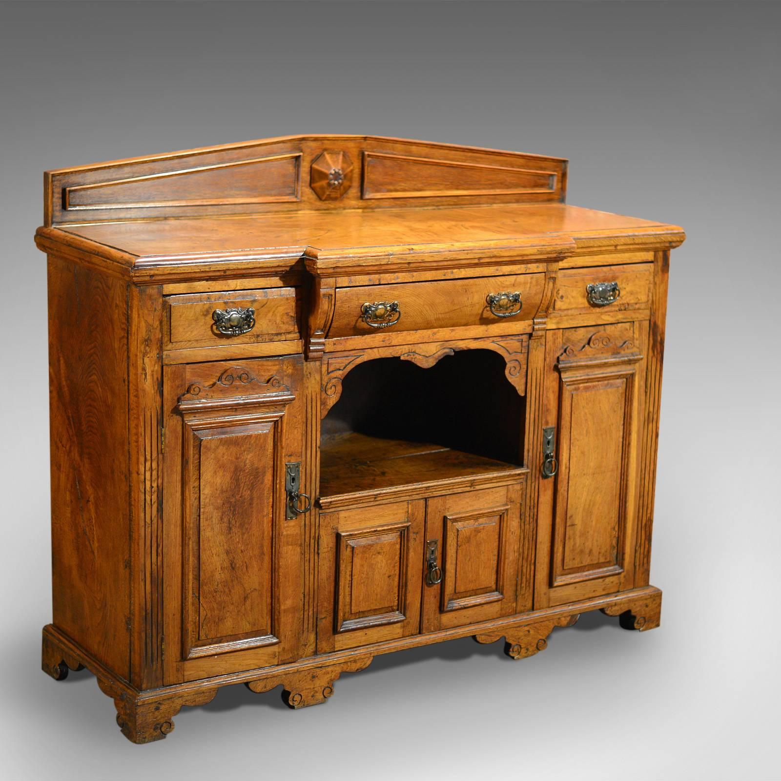 This is a small antique breakfront sideboard, circa 1900.

Expertly constructed in well figured, rustic, honey colored oak this modestly proportioned sideboard is raised on shaped bracket feet detailed with sinuous curves and carved spiraling