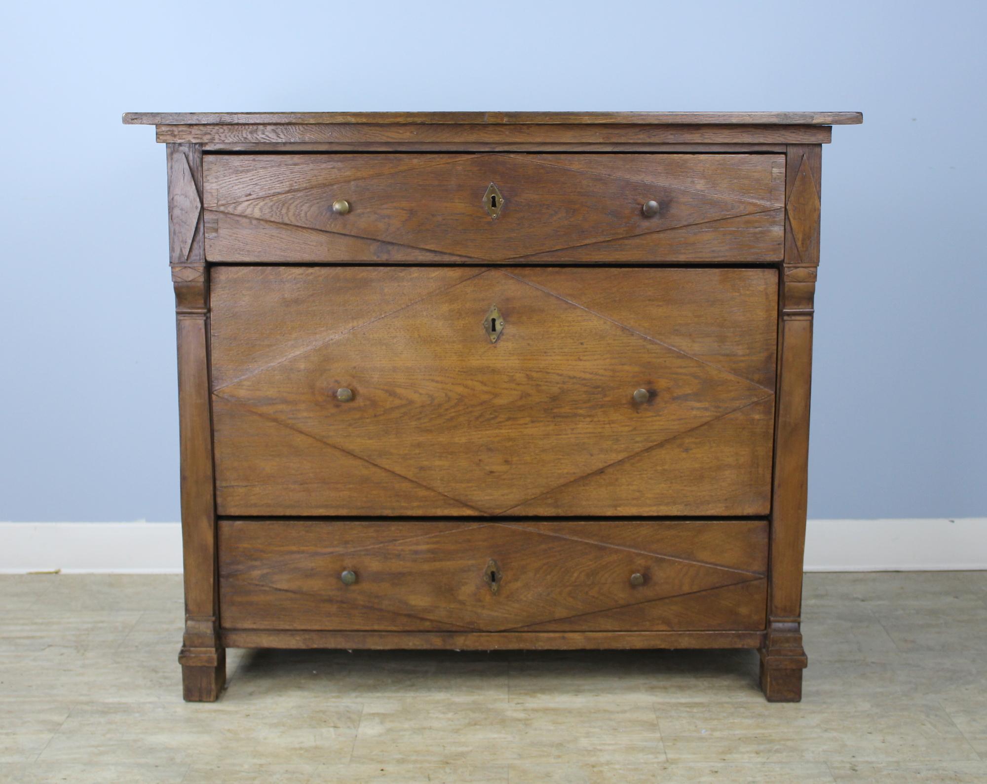 A handsome large French chest of drawers in dark chestnut. All three drawers display a typical diamond motif, the center drawer boasting a double depth. The top is in good antique condition with nice color and patina, and the stylized feet add to