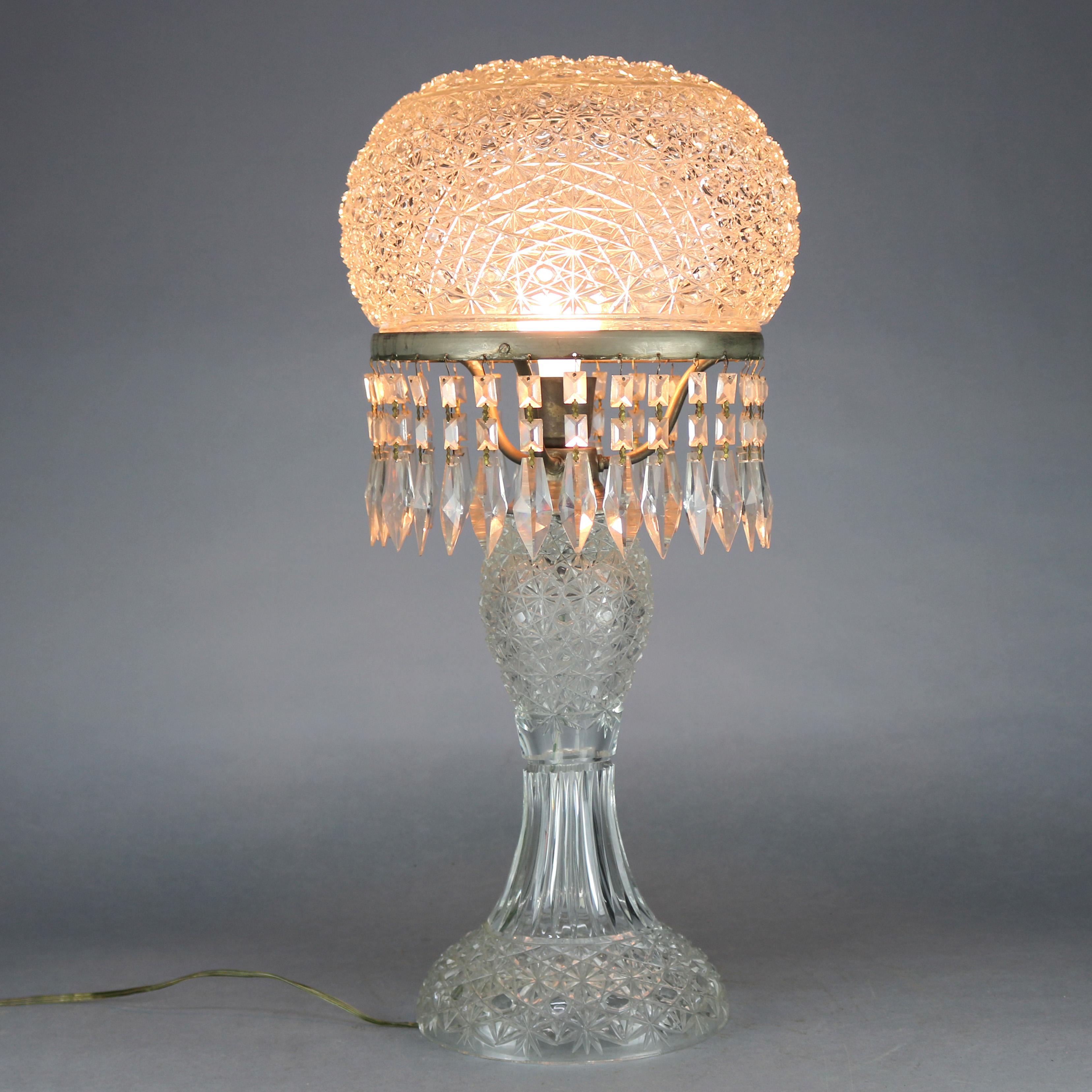 A large and antique brilliant cut glass mushroom parlor table lamp offers mushroom domed shade with hanging cut crystals and over hourglass base, circa 1920.

Measures: 27.25