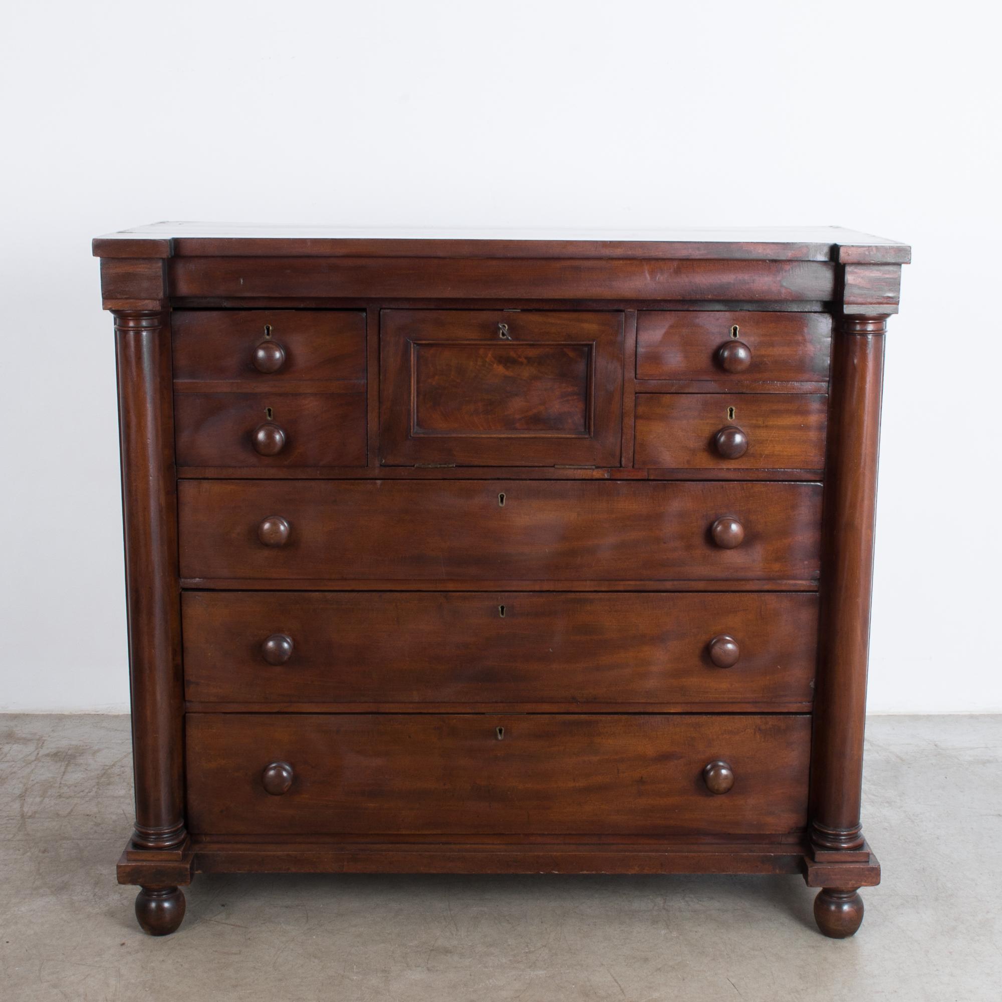 This wooden chest of drawers from the UK, circa 1880, features three full spacious drawers and a letter compartment, which folds down into a small writing surface, finished in green leather. On the right side of the letter compartment are two