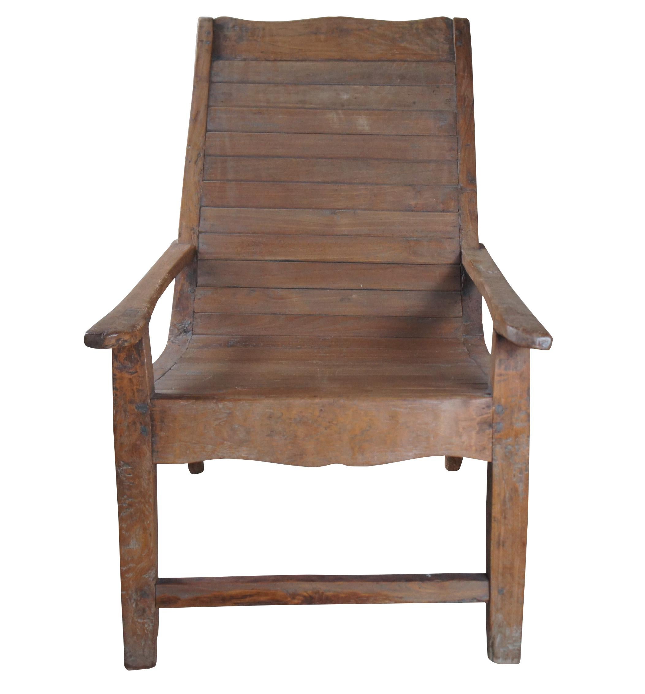 Early 20th century British Colonial Anglo Indian plantation chair. Made from teak in mortise and tenon joinery with a relaxed lounged frame and long arms. Features a curved crest rail and planked seat. Naturally distressed from use and