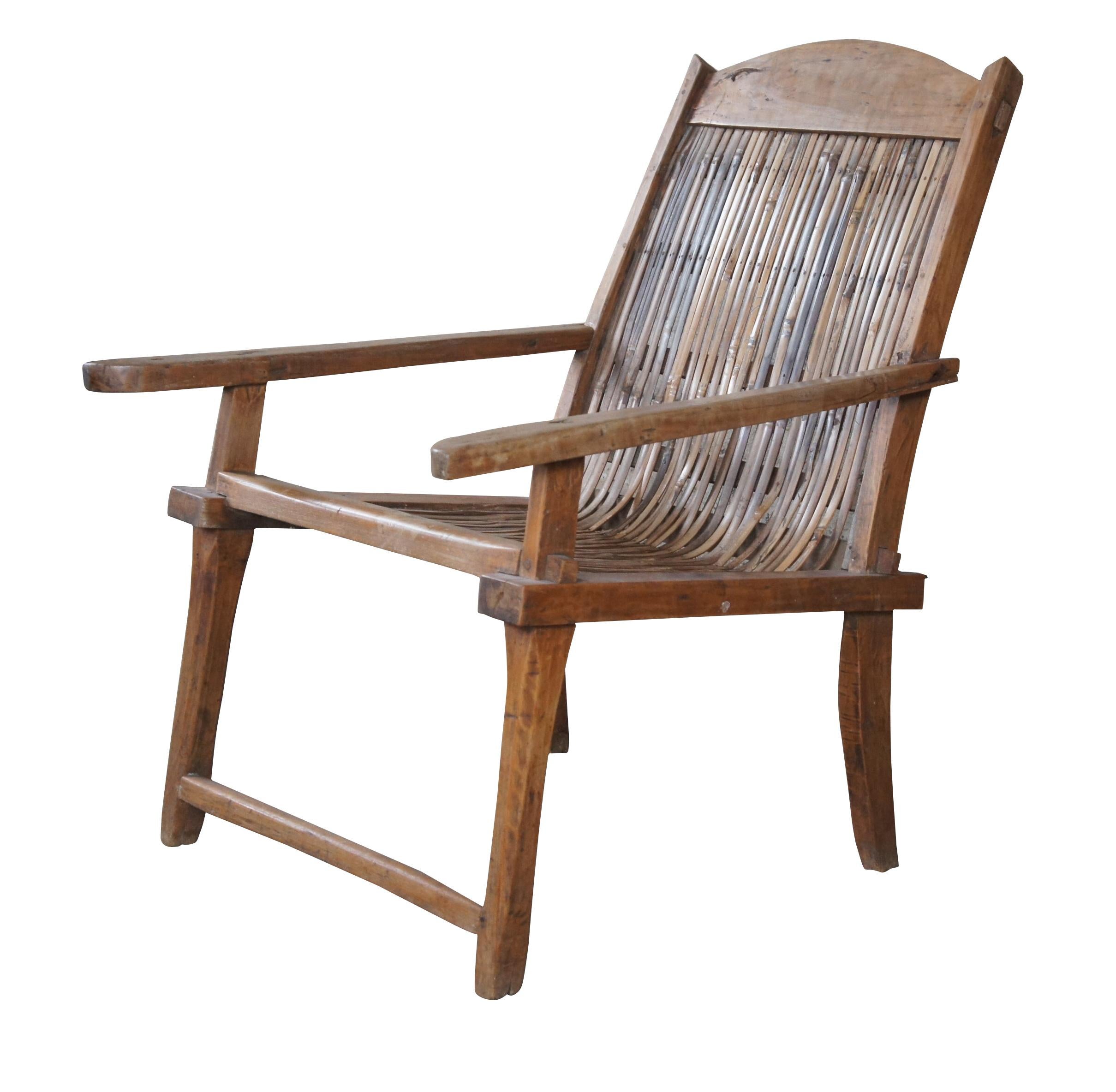 Early 20th century British Colonial Anglo Indian plantation chair. Made from teak in mortise and tenon joinery with a relaxed lounged frame and long arms. Features a curved crest rail and split reed bent rattan seat.

There's nothing better than