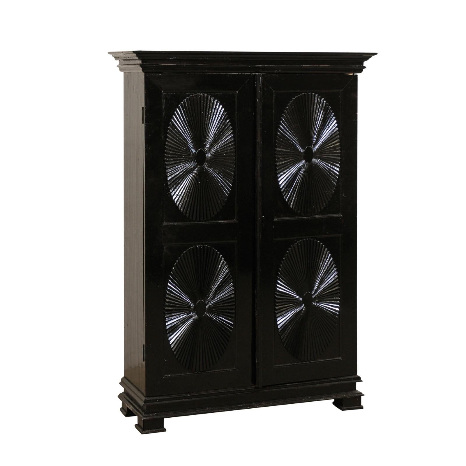 A British Colonial decoratively paneled two-door storage cabinet from the turn of the 19th and 20th century. This antique cabinet from India features a pair of tall raised-panel doors, each adorn with two fan-carved ovals, one atop the other, and