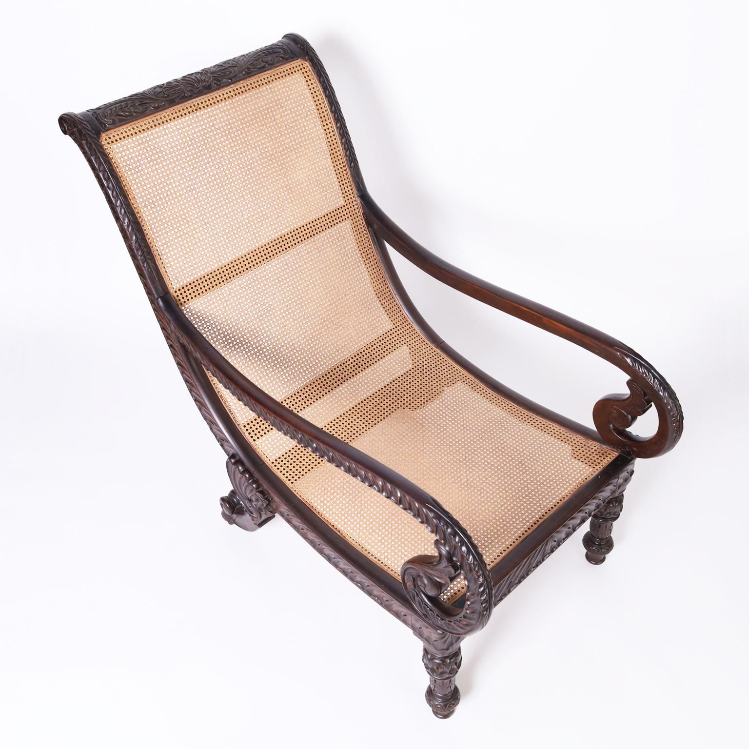 Impressive British Colonial plantation chair crafted in mahogany in a graceful form with dramatic carved ocean and floral motifs on the back and rolled arms, having caned seat and back and legs carved with acanthus and sea shell designs.