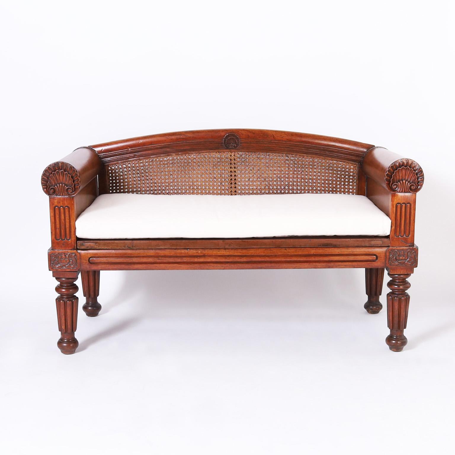 Impressive 19th century British Colonial settee handcrafted in mahogany with a caned back and seat featuring sea shell carvings on the back and arms, floral carvings on the knees and bold turned and beaded legs.