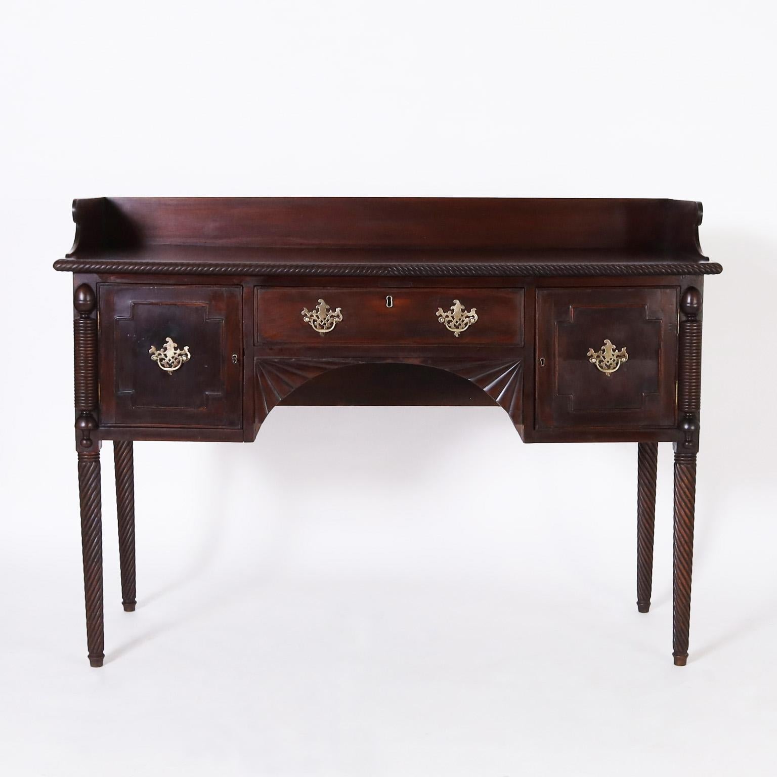 Rare and Remarkable 19th century British colonial server handcrafted in mahogany with a dark lush finish featuring a classic gallery on the top, two doors and a drawer, brass hardware, fan brackets and elegant turned and twisted legs.