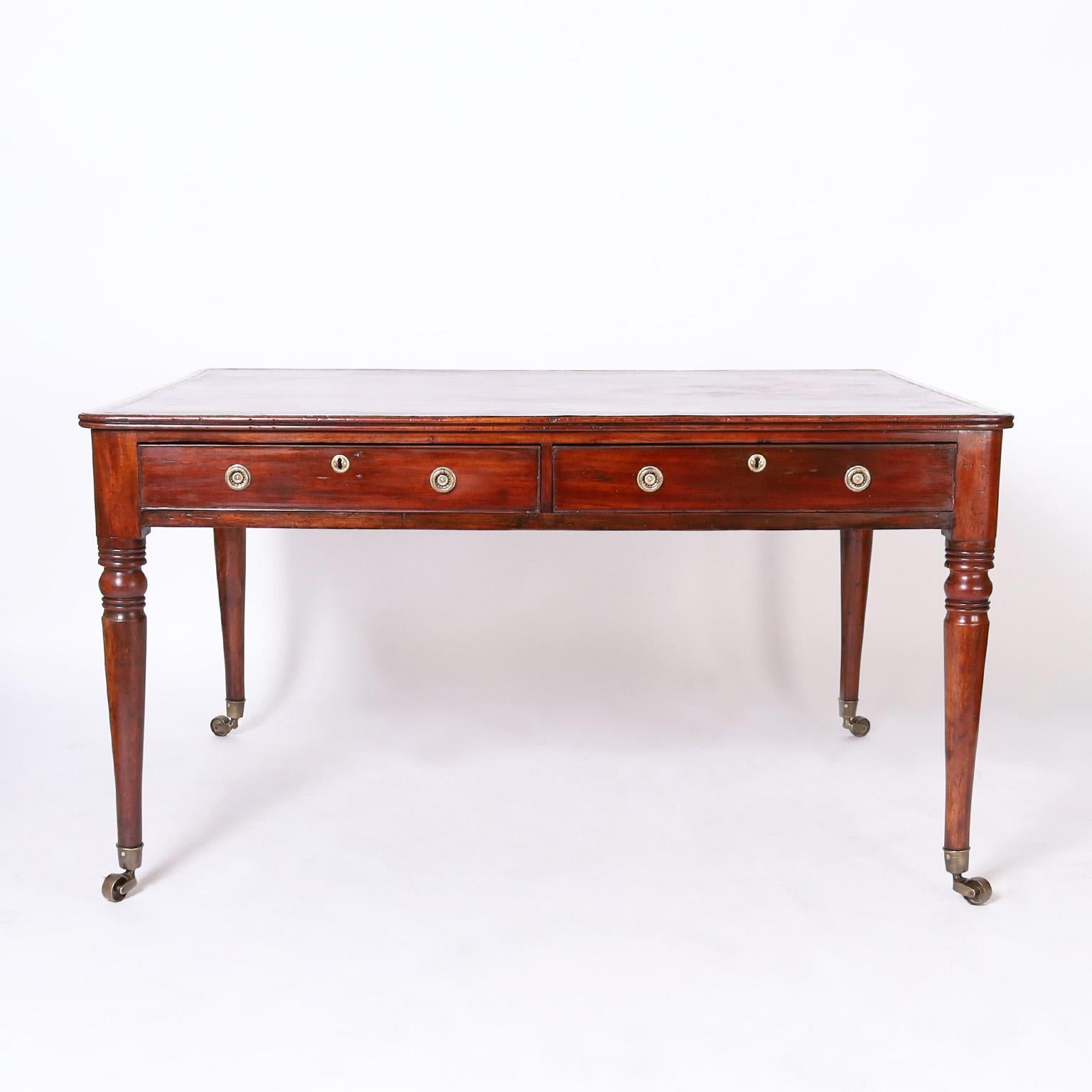 Atractivo escritorio de socios British Colonial fabricado a mano en caoba con tapa de cuero marrón labrado, dos cajones a cada lado y elegantes patas torneadas sobre ruedas de latón.