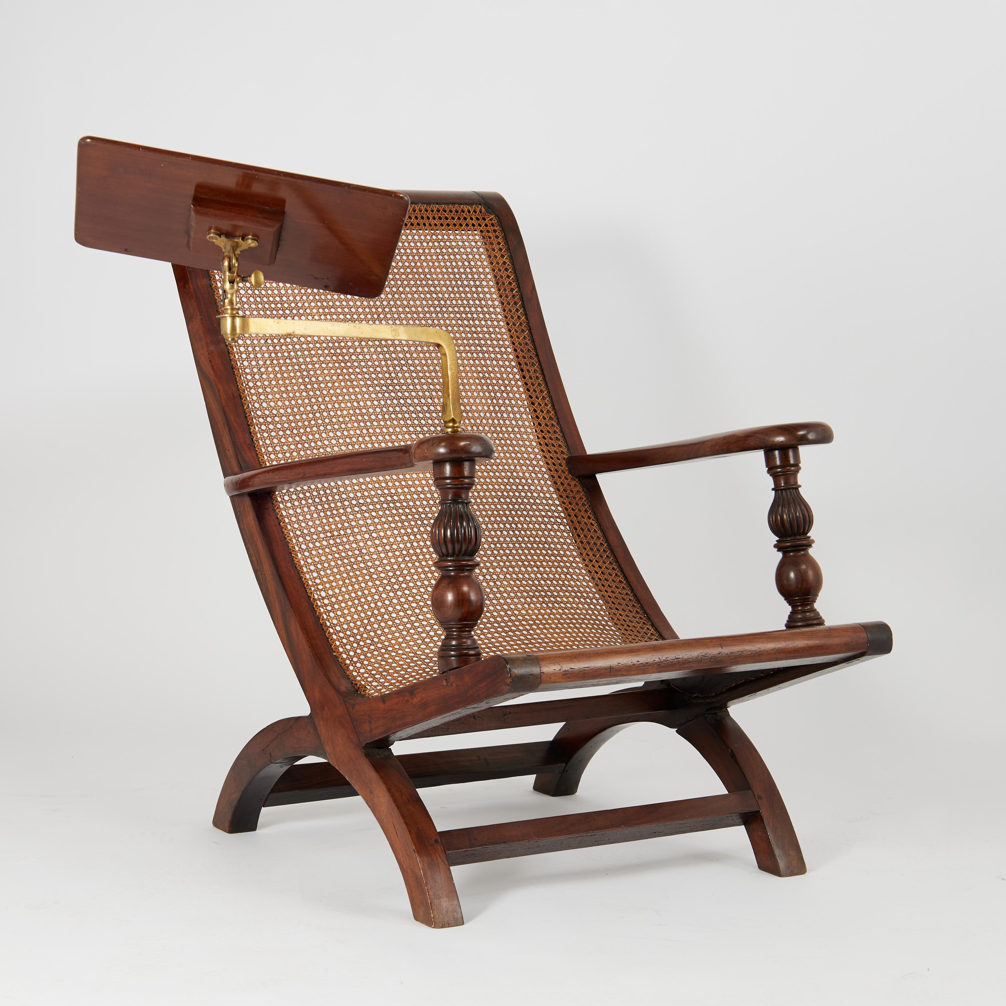 Rare and remarkable 19th Century English colonial plantation chair handcrafted in mahogany in elegant form, featuring a caned seat, turned and beaded arm supports and a book stand with an adjustable brass support mechanism. 

