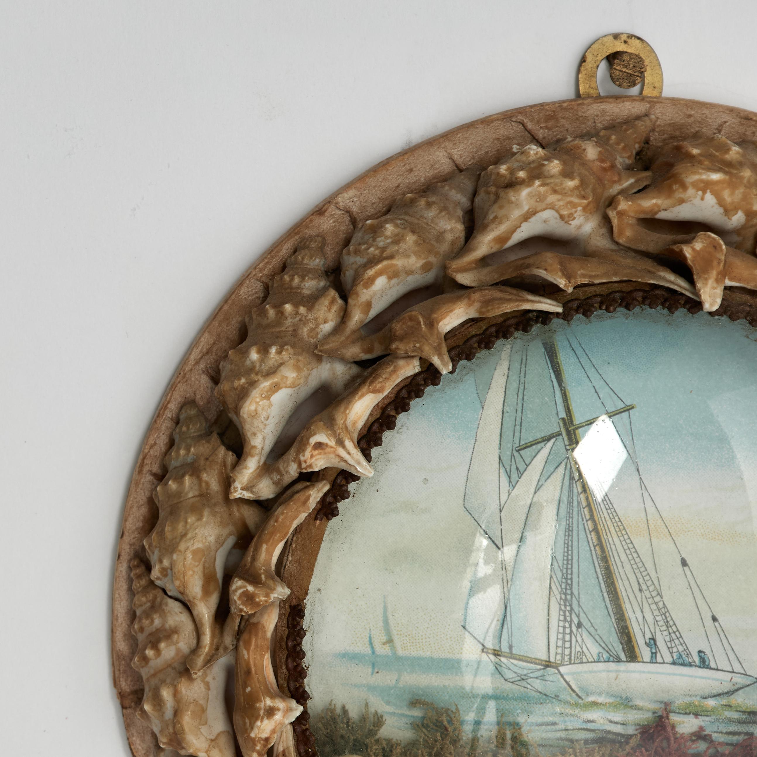 Enchanting early 20th century British colonial sailors valentine handcrafted in exotic seashells around an image of a schooner or sailboat as seen through a convex glass lens.
