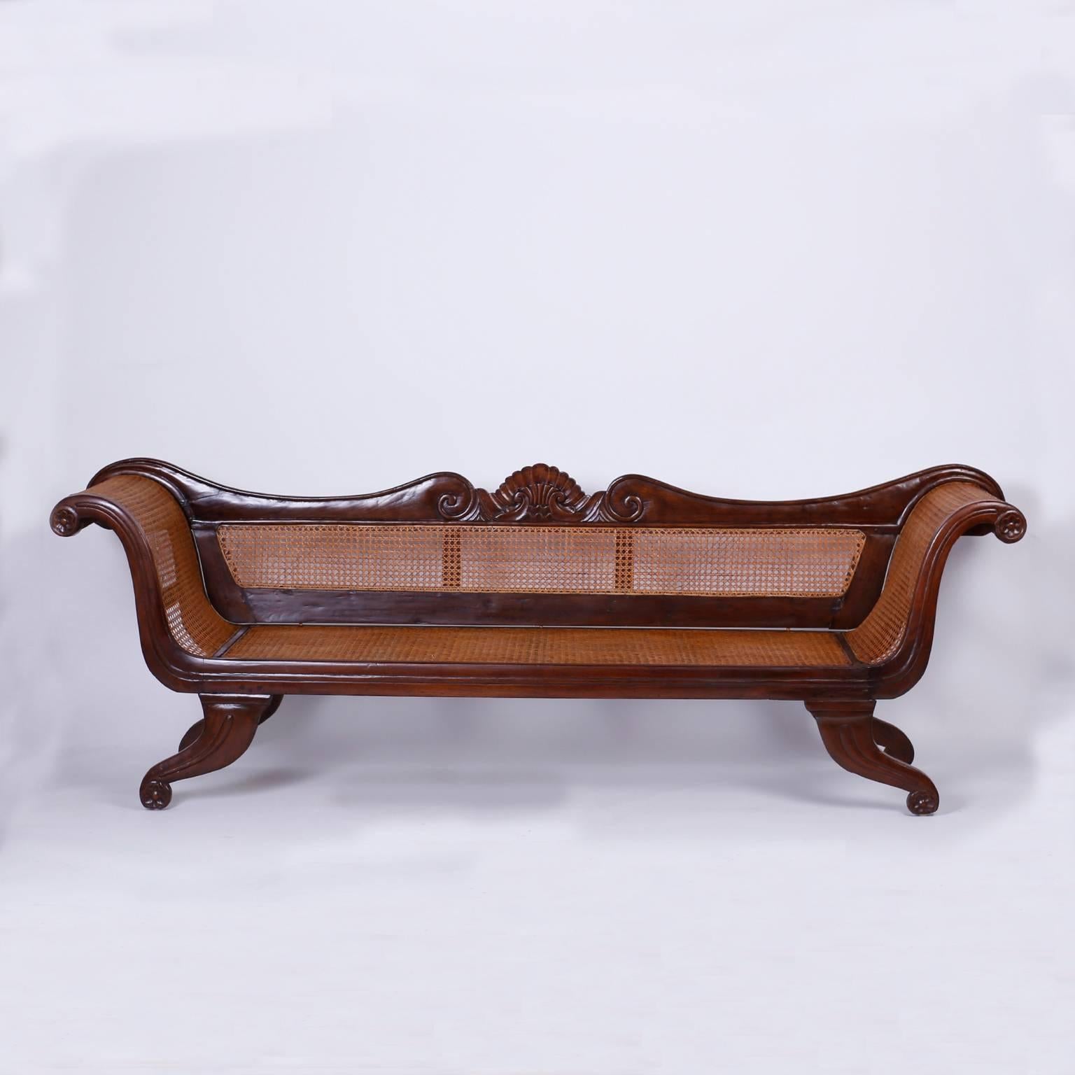 Fine antique British colonial settee with a graceful poetic form. The mahogany frame is beautifully carved with waves and seashells on paw feet. The back, seat, and arms are hand caned typical of tropical furniture of the West Indies. The
