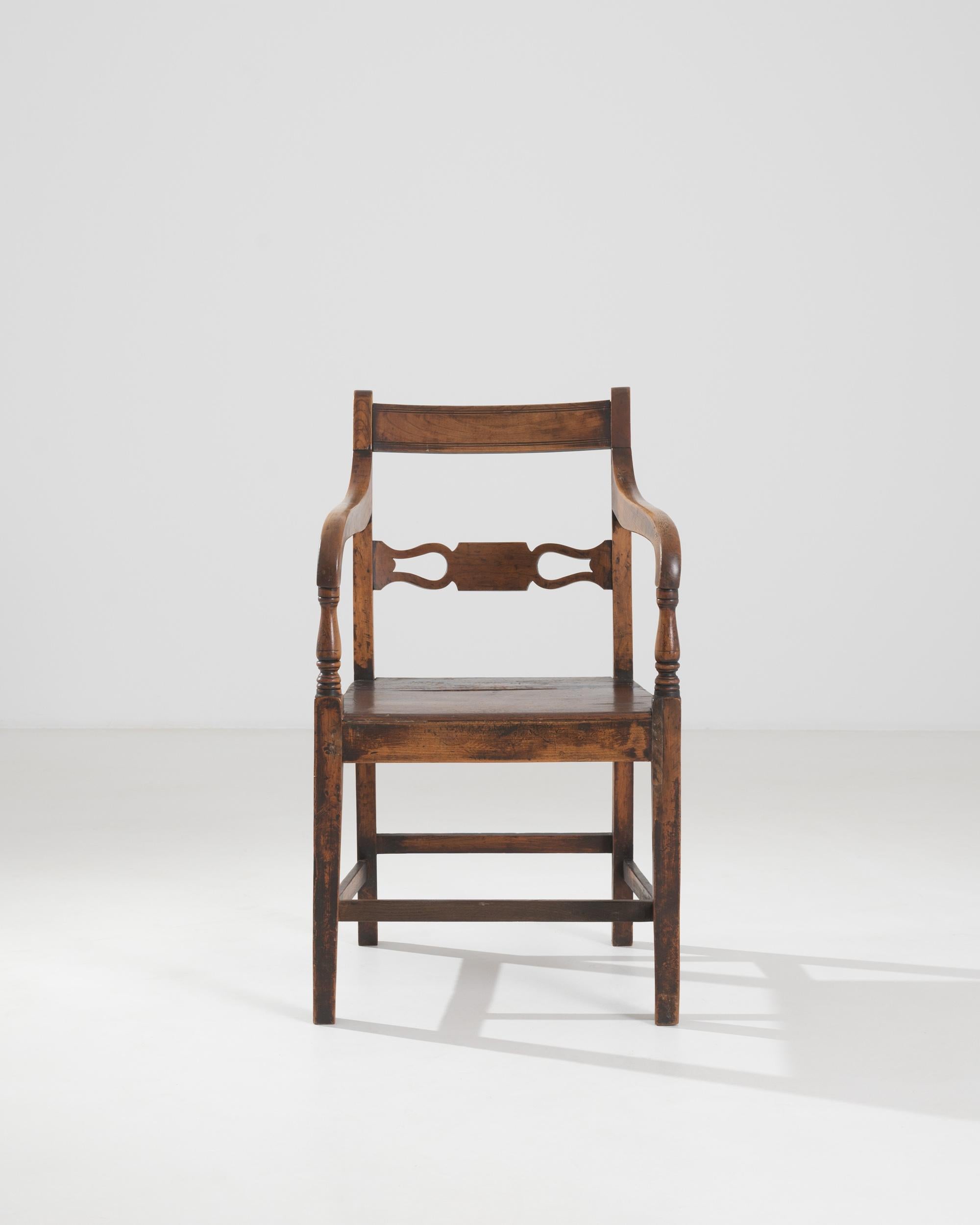 A British chair from the 19th century. This wooden chair offers a comfortable and elevated moment of rest. The carved back curves ergonomically, while sloping arm rails and square legs create a harmonious synergy throughout its construction. Its