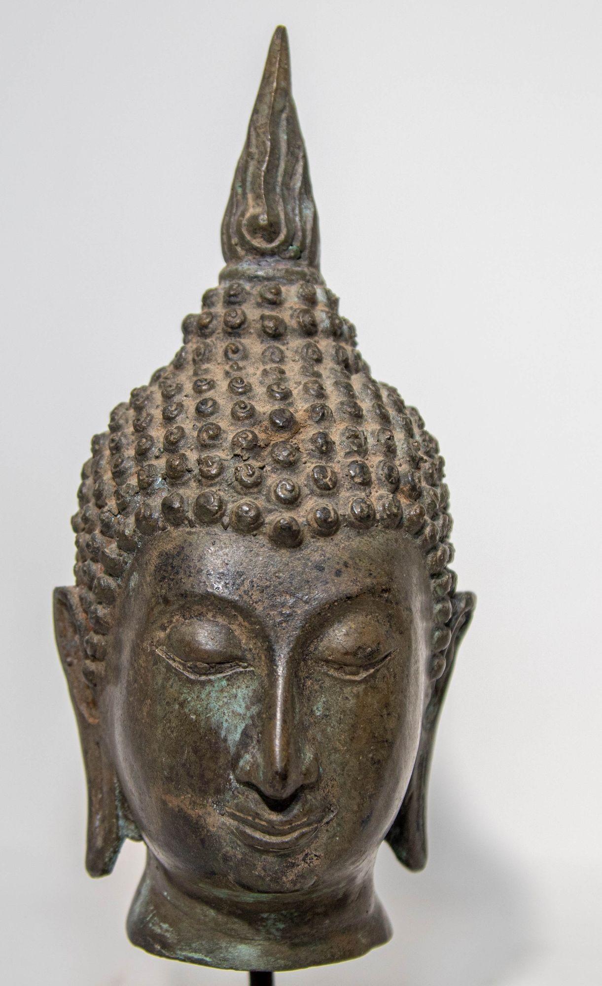 Sculpture ancienne en bronze à tête de bouddha du Sud-Est asiatique, patinée vert-de-gris, montée sur un socle en bois à base noire.
Tête de Bouddha en bronze de style Sukhothai à patine verte, provenant du nord de la Thaïlande.
La tête est