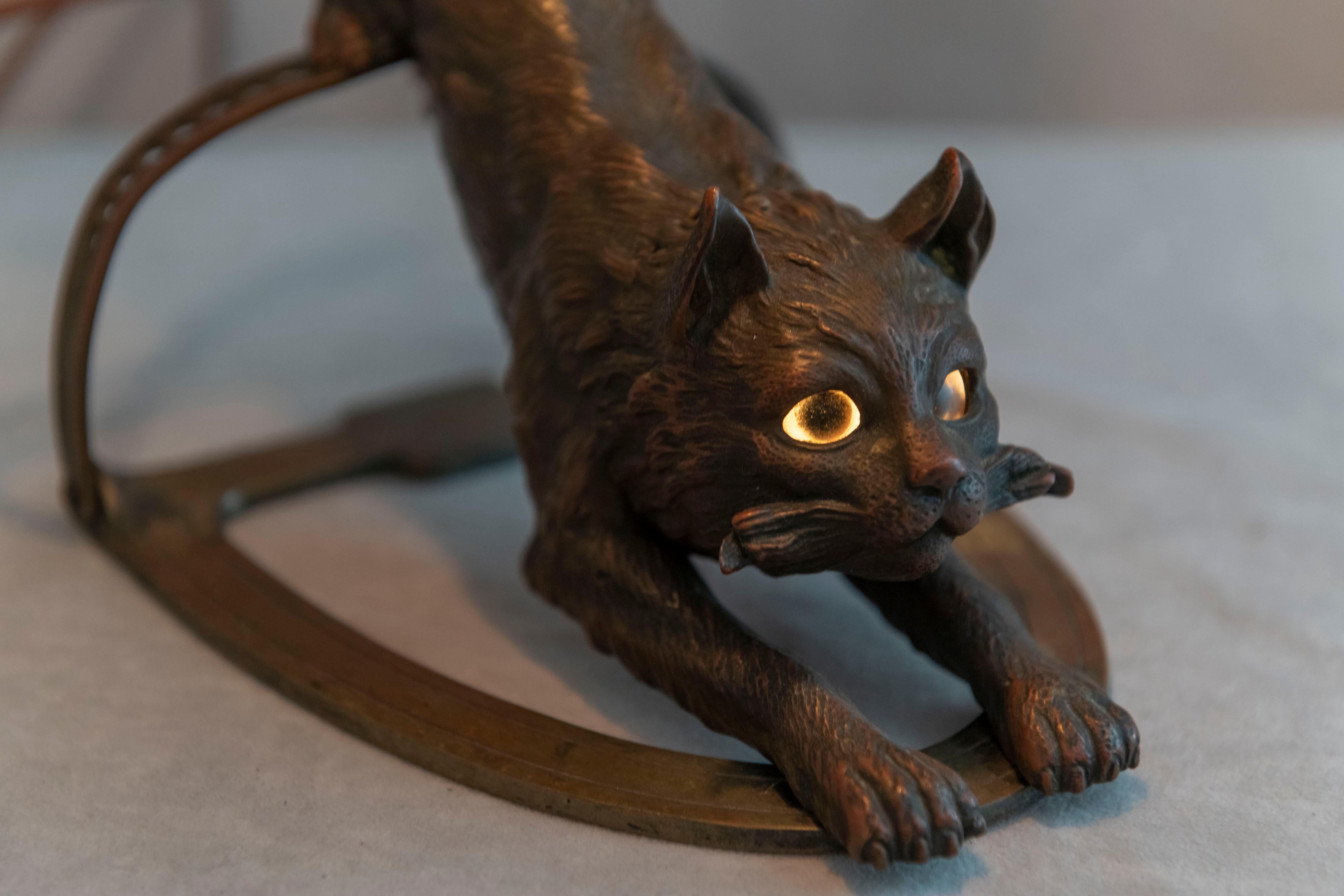  This whimsical lamp is not only for cat lovers, but anyone who appreciates fine workmanship and the unusual. The cat on all fours is obviously avoiding the trap while the shade shows smiling cat faces. It's all done in a rich brown patina. The eyes