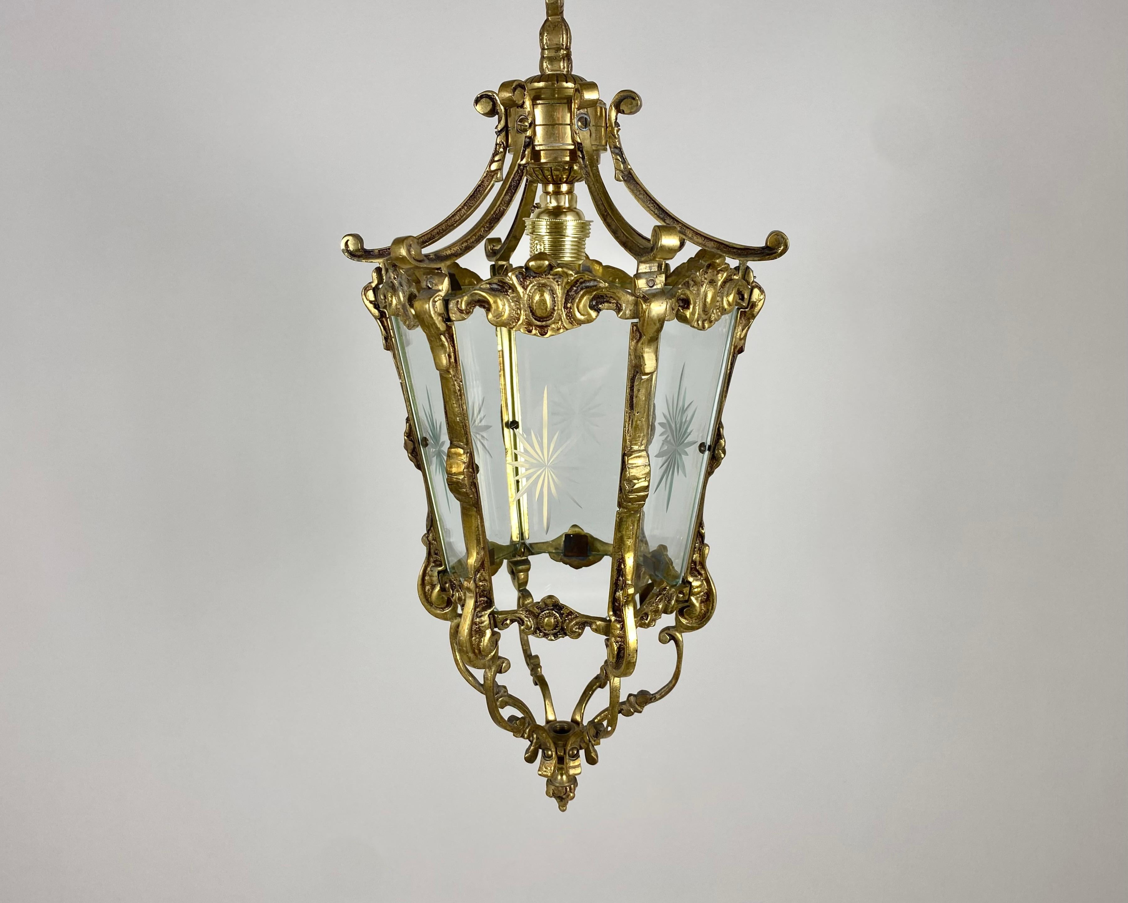 Antique gilded bronze hall lantern with one lamp surrounded by sectional tapering glass panels and held within a foliated scrolling framework with decorative central pierced leaves and open scrolling canopy, having the original chain and ceiling