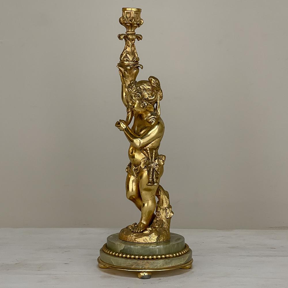 Antique bronze D'Ore Cherub Statue on Onyx candlestick celebrates classic beauty! The representation of an innocent cherub clothed in vines and wearing a flower garland and carrying a pan flute shows the figure holding aloft a torchere which leads