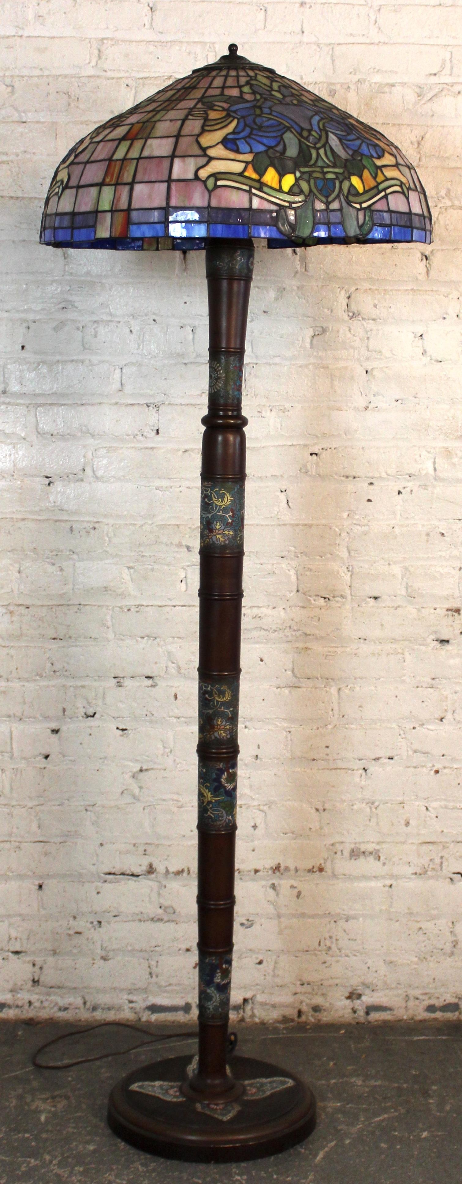 Lampada da terra antica in stile Tiffany con paralume in vetro colorato con intricati motivi floreali. La base in metallo ornato completa la lavorazione artigianale del vetro, proiettando una calda luce d'ambiente. Un pezzo senza tempo che dona a