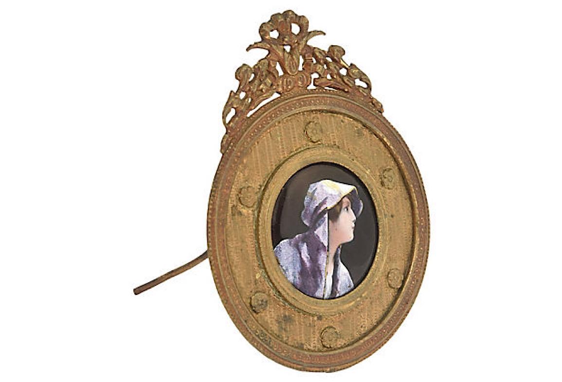 Enamel painting of a woman's profile on copper set in an ornate bronze frame. The back has an easel as well a ring so it can be set on a table or mounted on the wall. Age wear, tarnished, light scratches.