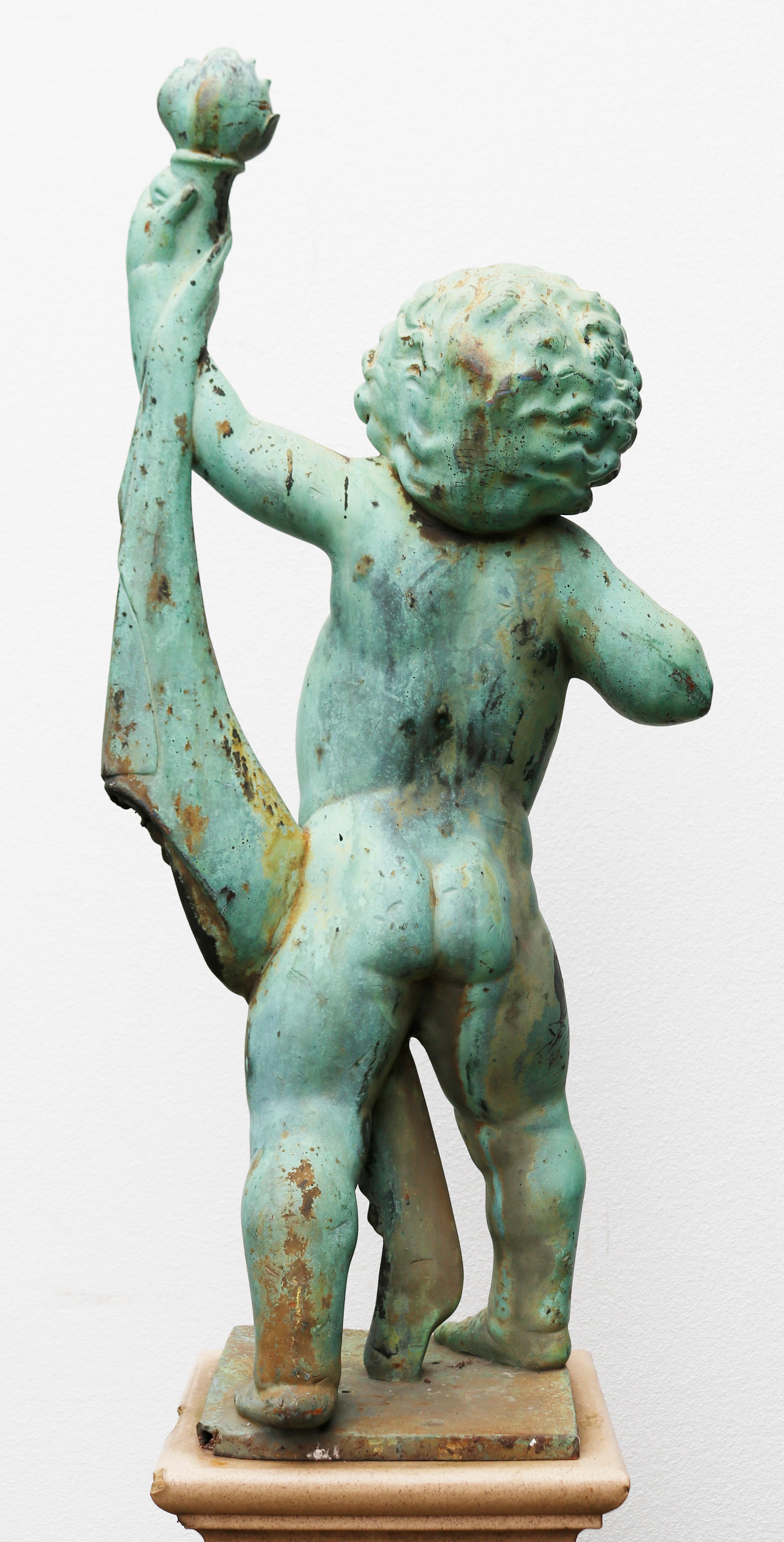 Antique bronze garden statue of a Putto. A verdigris patinated bronze model of a touch bearing putto. Standing on a glazed ceramic pedestal. Indistinct makers stamp to base.