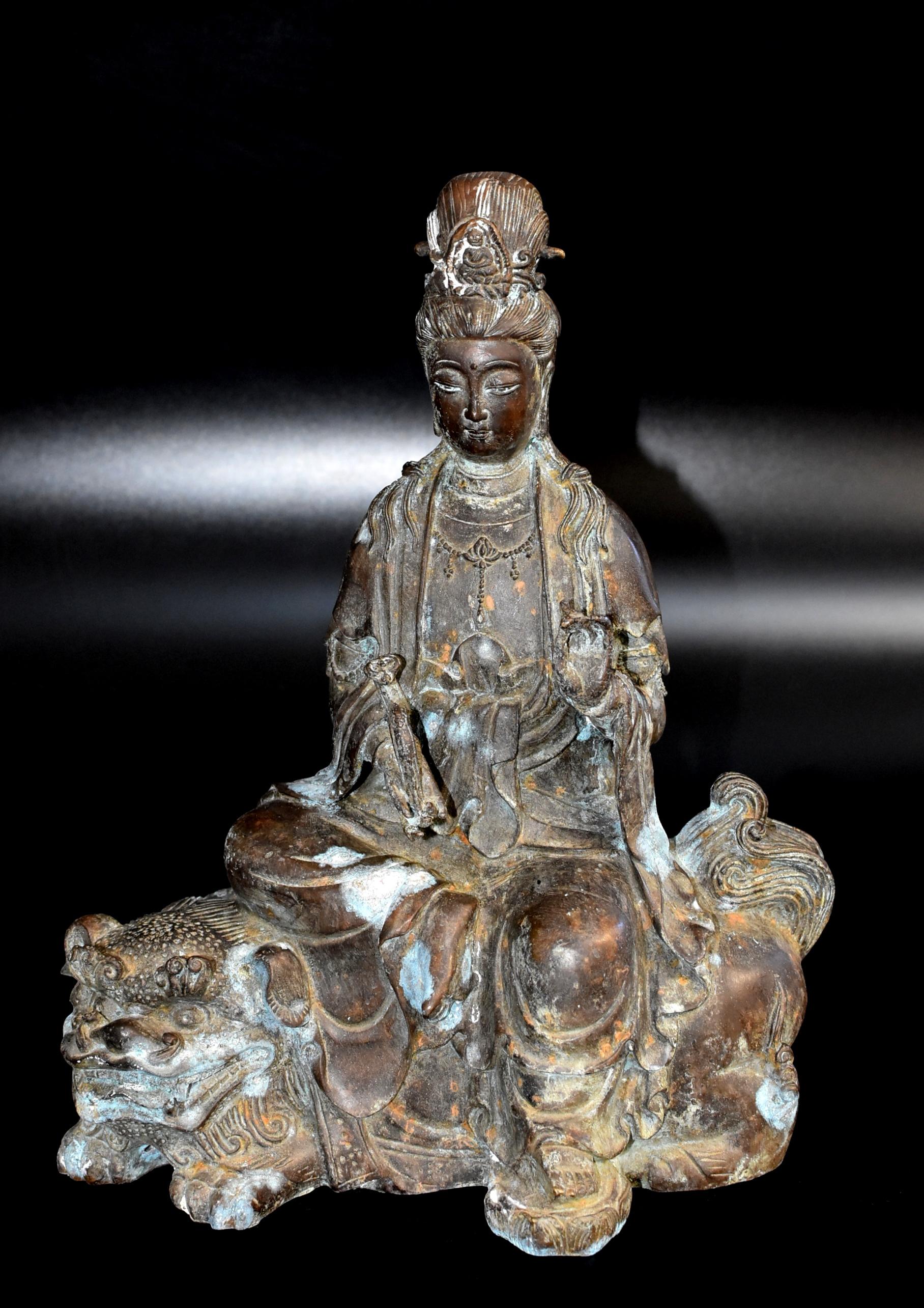 A wonderful old piece of bronze sculpture featuring the Chinese Goddess of Compassion Guan Yin, Bodhisattva Avalokiteshvara. Seated on a recumbent Foo Dog lion, the figure rendered a serene expression framed by a pair of long earlobes, the downcast
