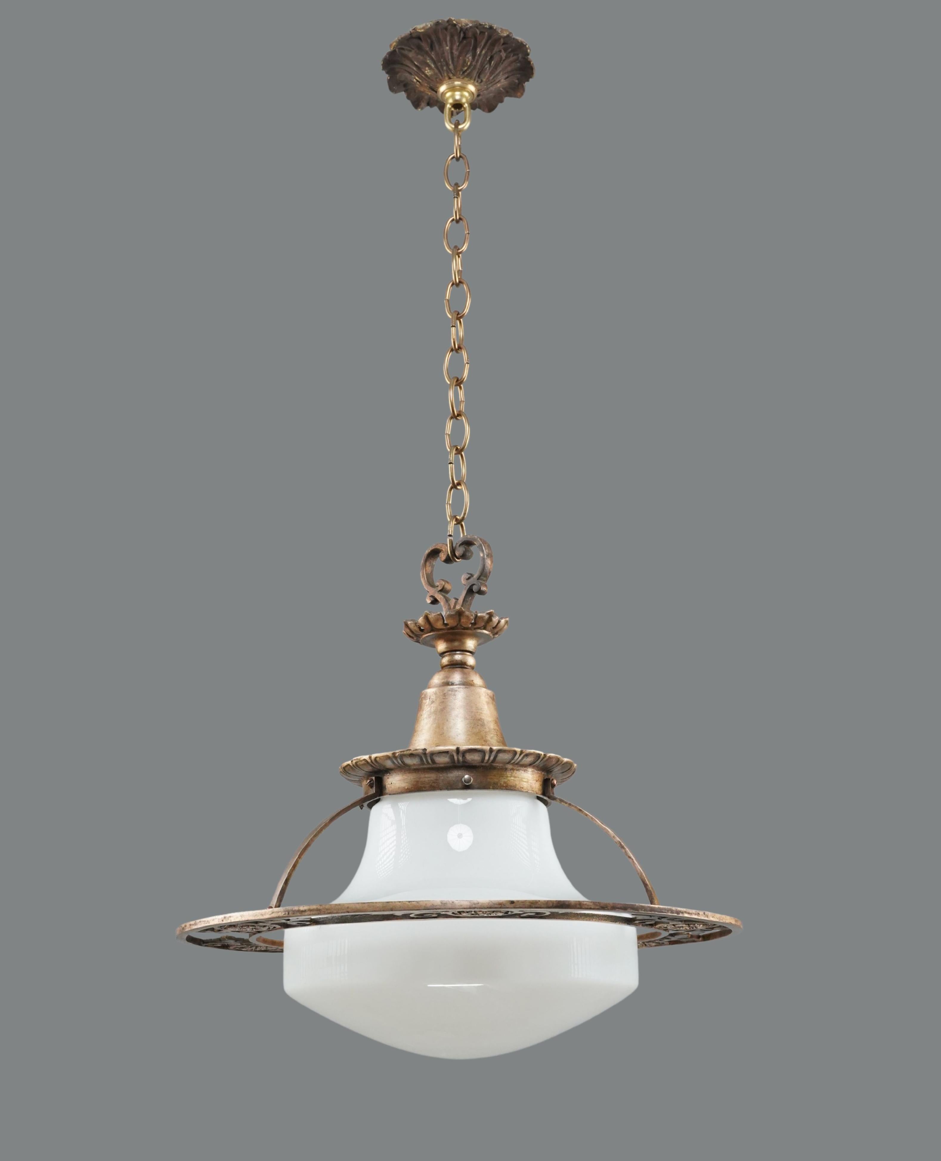 Lampe suspendue du début du 20e siècle avec un globe en verre au lait blanc et une chaîne en bronze. Le cadre en bronze est orné de volutes et d'éléments floraux. La chaîne est en acier. Cette lampe nécessite une ampoule standard à culot moyen de