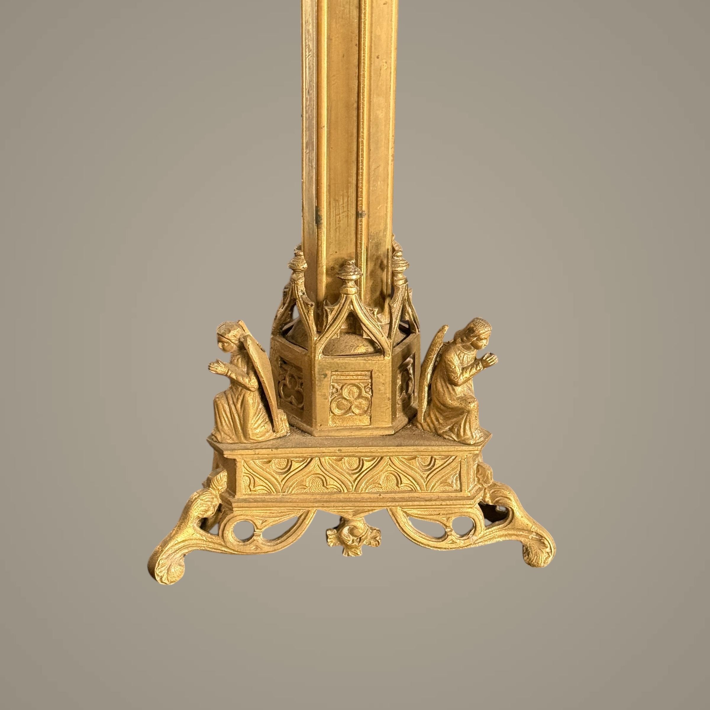 Questo squisito candeliere neogotico in bronzo dorato è un vero capolavoro di artigianato, che incarna l'intricata eleganza dell'arte ecclesiastica e decorativa del XIX secolo. Poggiato con grazia su una base robusta e decorata, è ornato da tre