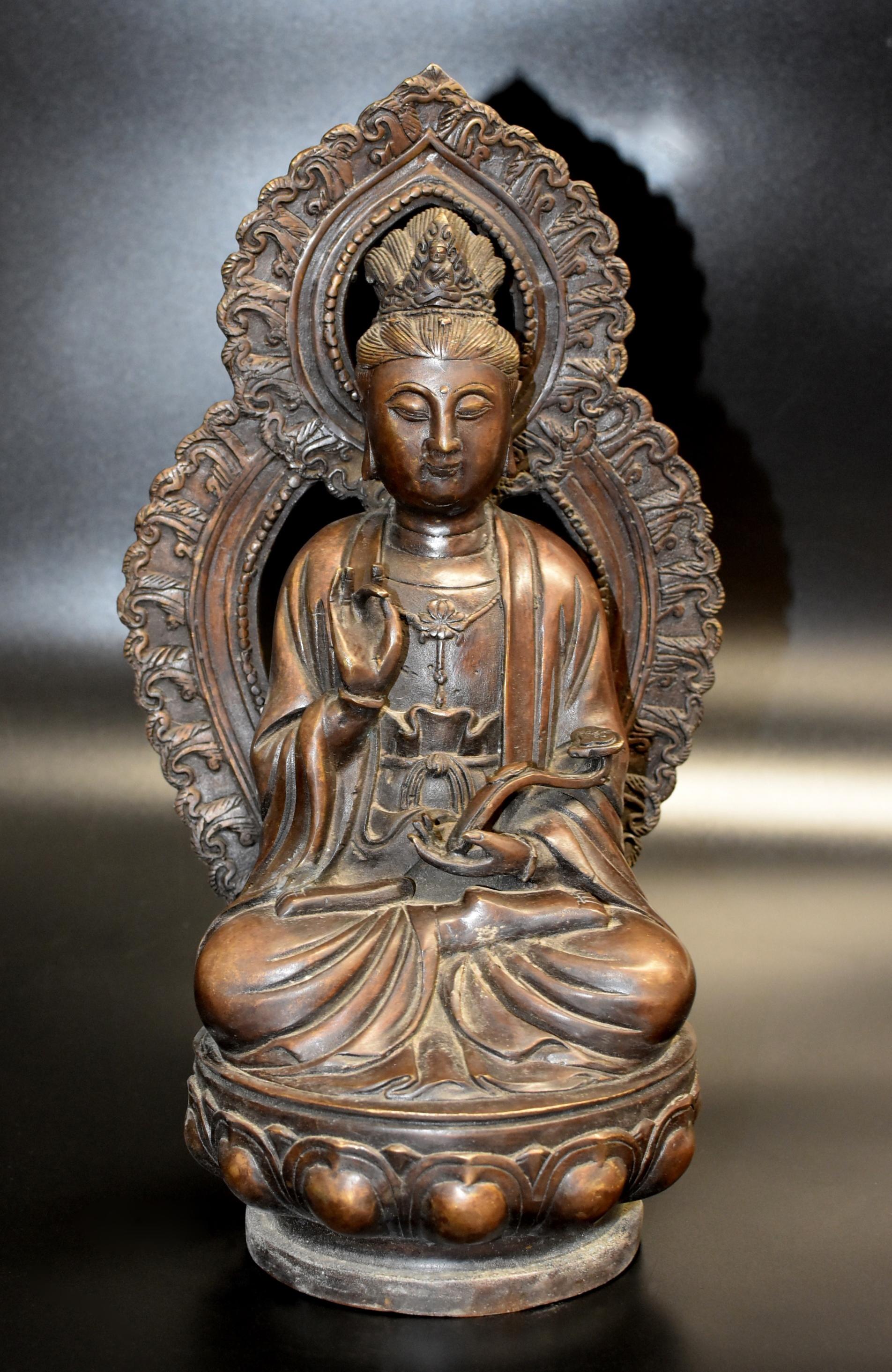 A beautiful bronze Guan Yin, Bodhisattva Avalokiteshvara, Goddess of Great Compassion. Seated on a lotus base against a flame-shaped mandorla, the figure rendered with a serene expression framed by a pair of pendulous earlobes, with downcast eyes