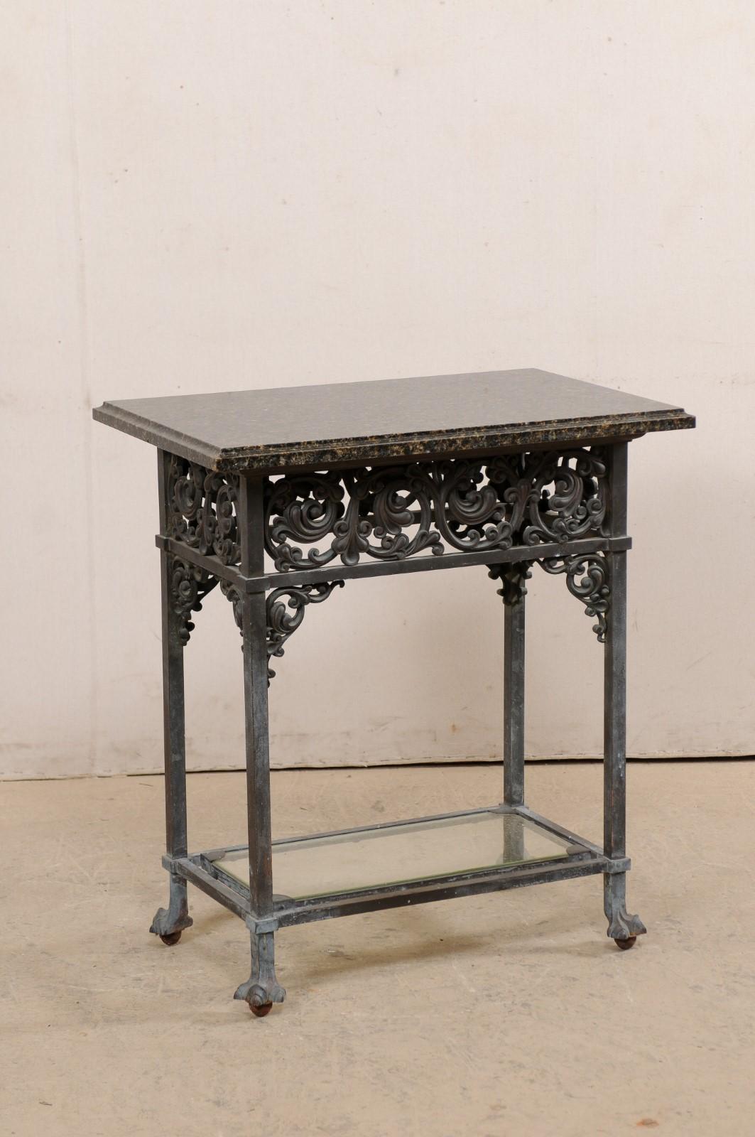 An American bronze table with acanthus leaf motif, granite top, and lower shelf, circa 1920's. This antique rectangular-shaped occasional table features its original granite top. It has an elaborately adorned thick skirt in a swirling acanthus leaf