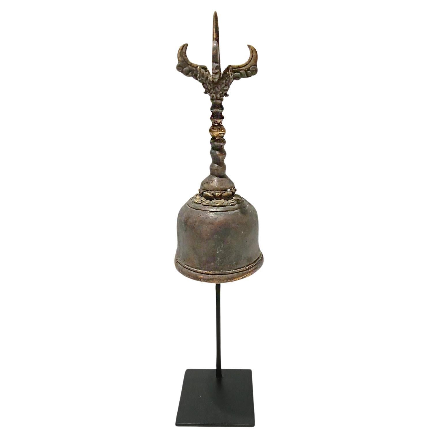 An antique bronze temple bell, hand-crafted in Indonesia, late 19th Century. Fully functional, emitting a clear, distinctive ring. The top of the bell contains a decorative design. 

The bell proper is 3 inches in diameter by 7.5 inches high. It is