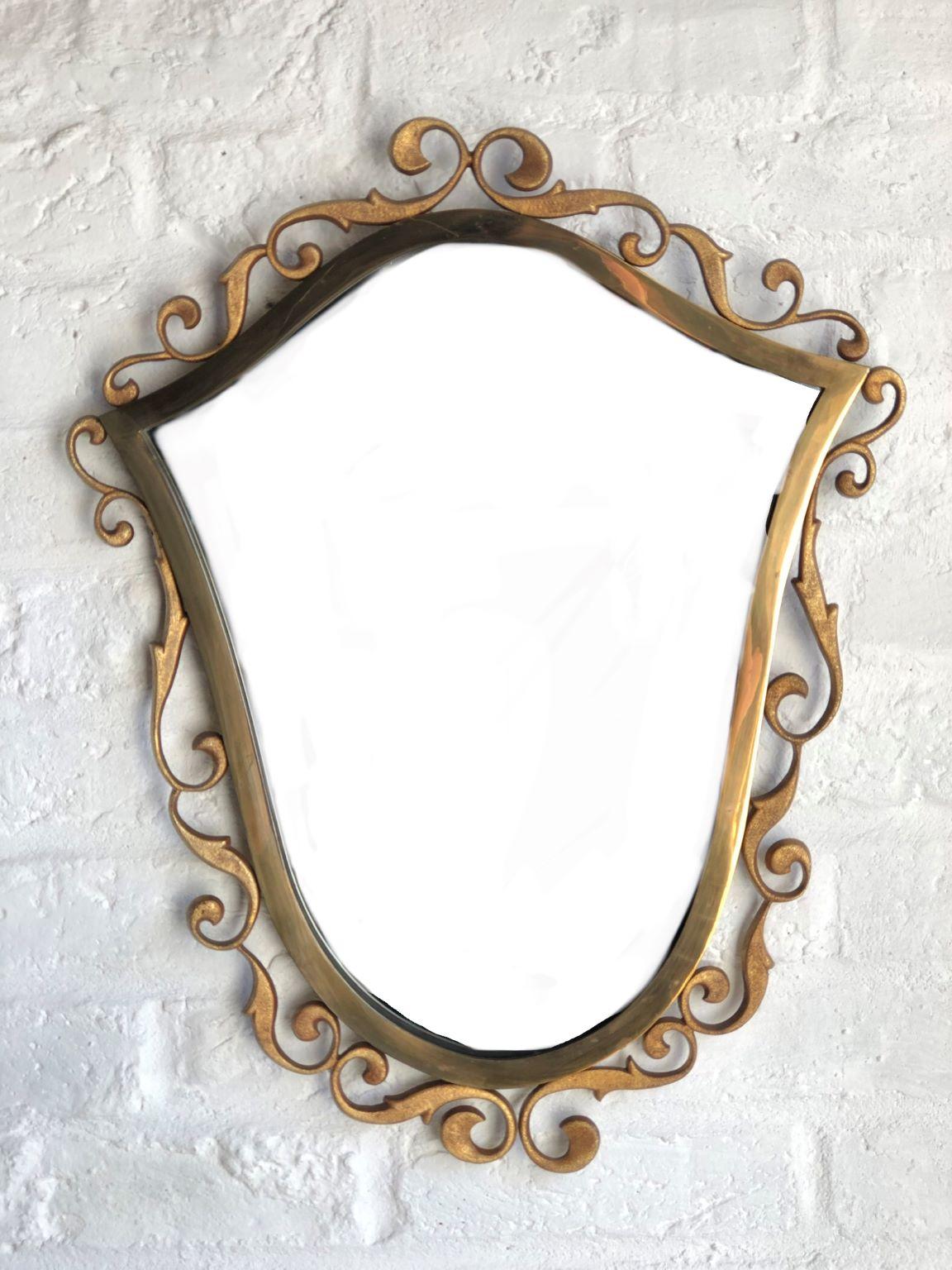 A beautiful Mid century bronze wall mirror signed by Moderna, Italy, 1940s

Elegant shield shape frame which is a combination of textured and polished surfaces.
Outer edge is adorned with scrolling shapes that are not quite symmetrical, which adds