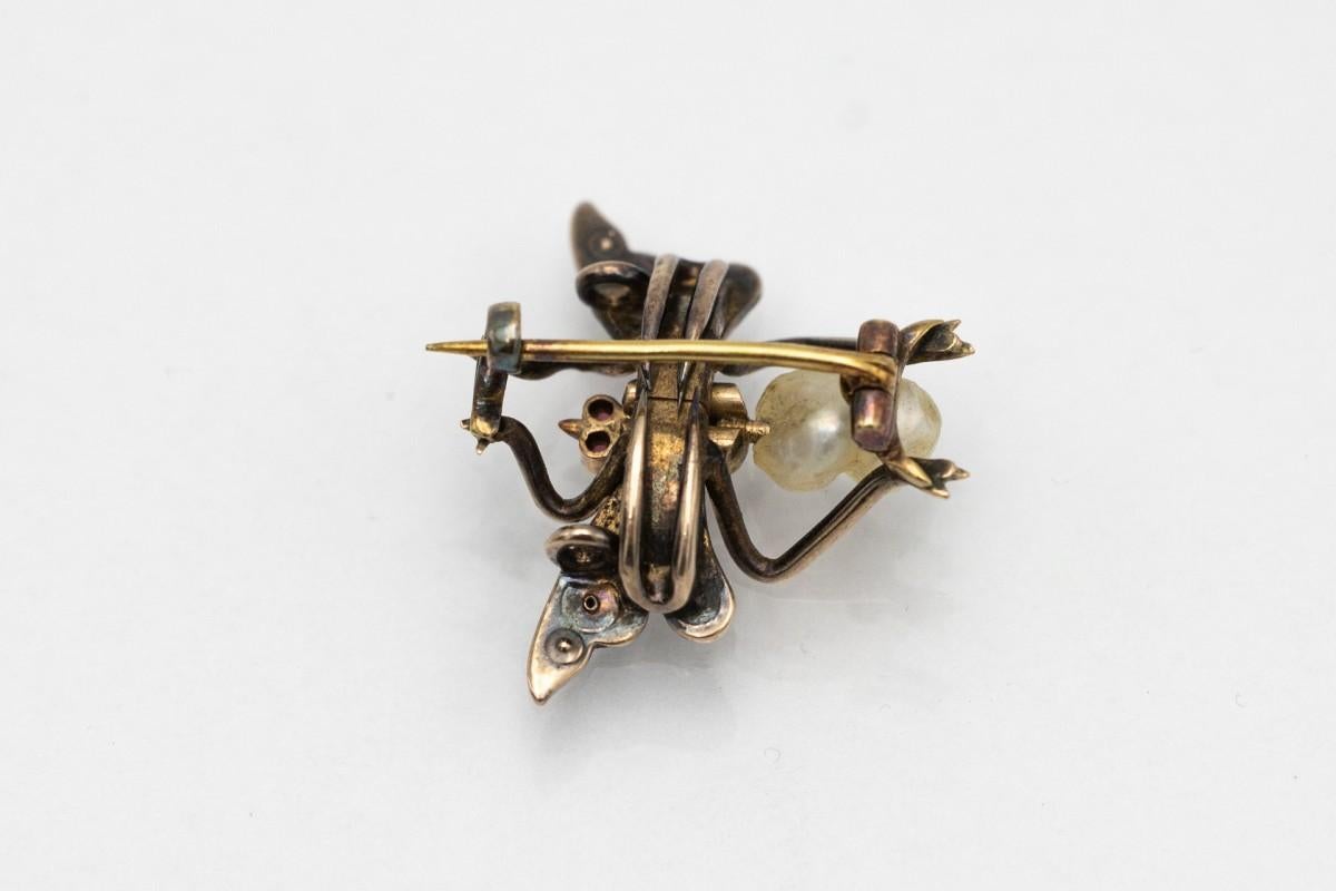 Antique insect brooch, made of 585/14K gold.
Total weight: 3.5g.
Origin: late 19th century.
Brooch in the shape of a fly, body made of two natural pearls, wings set with 14 diamonds of various sizes, two rubies as eyes.
Dimensions: 21.5 x 25.1 mm.