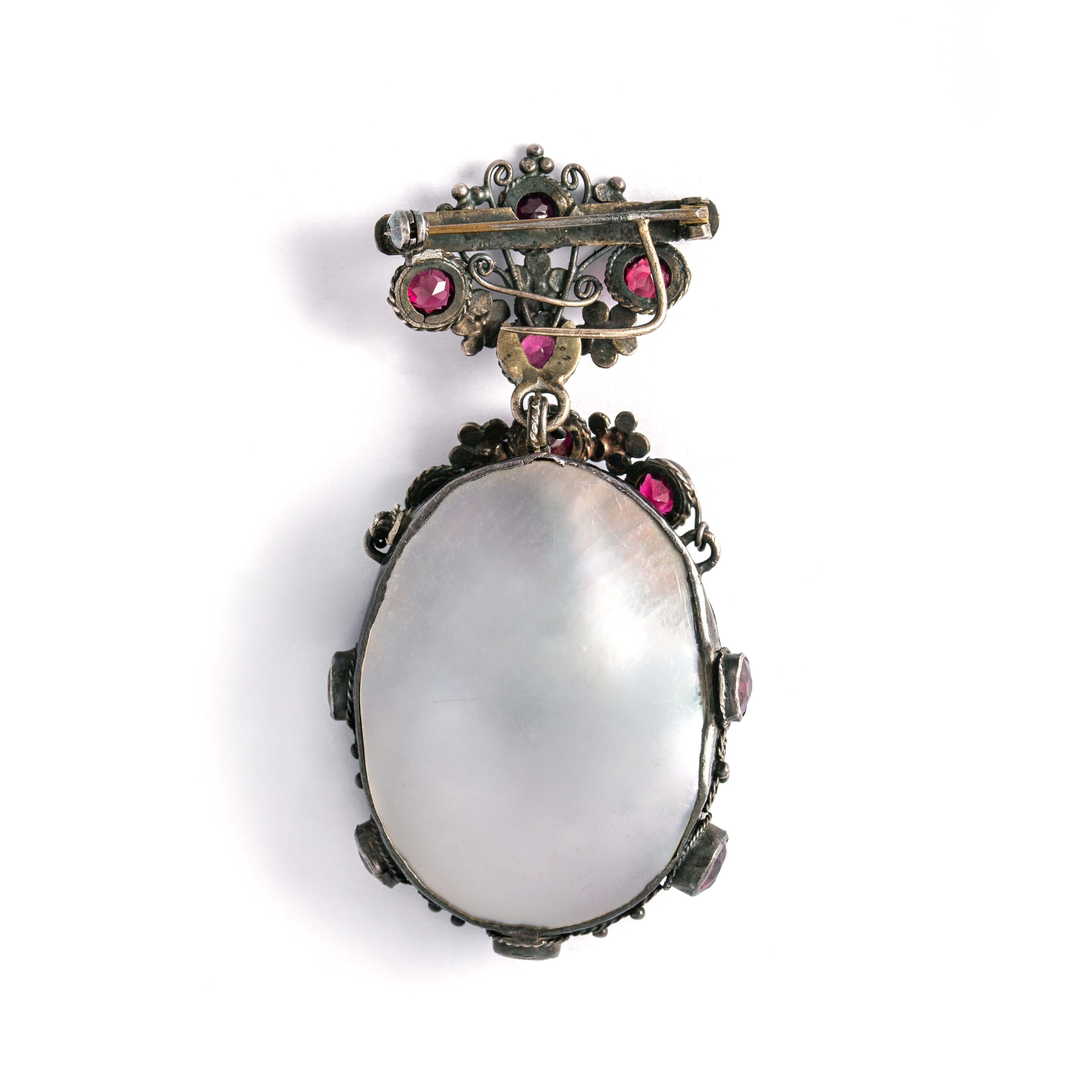 Antique Silver brooch set with red stones and holding a double-sided mother-of-pearl design.
Dimensions: 7.00 x 3.50 centimeters. 
Gross weight: 26.72 grams.