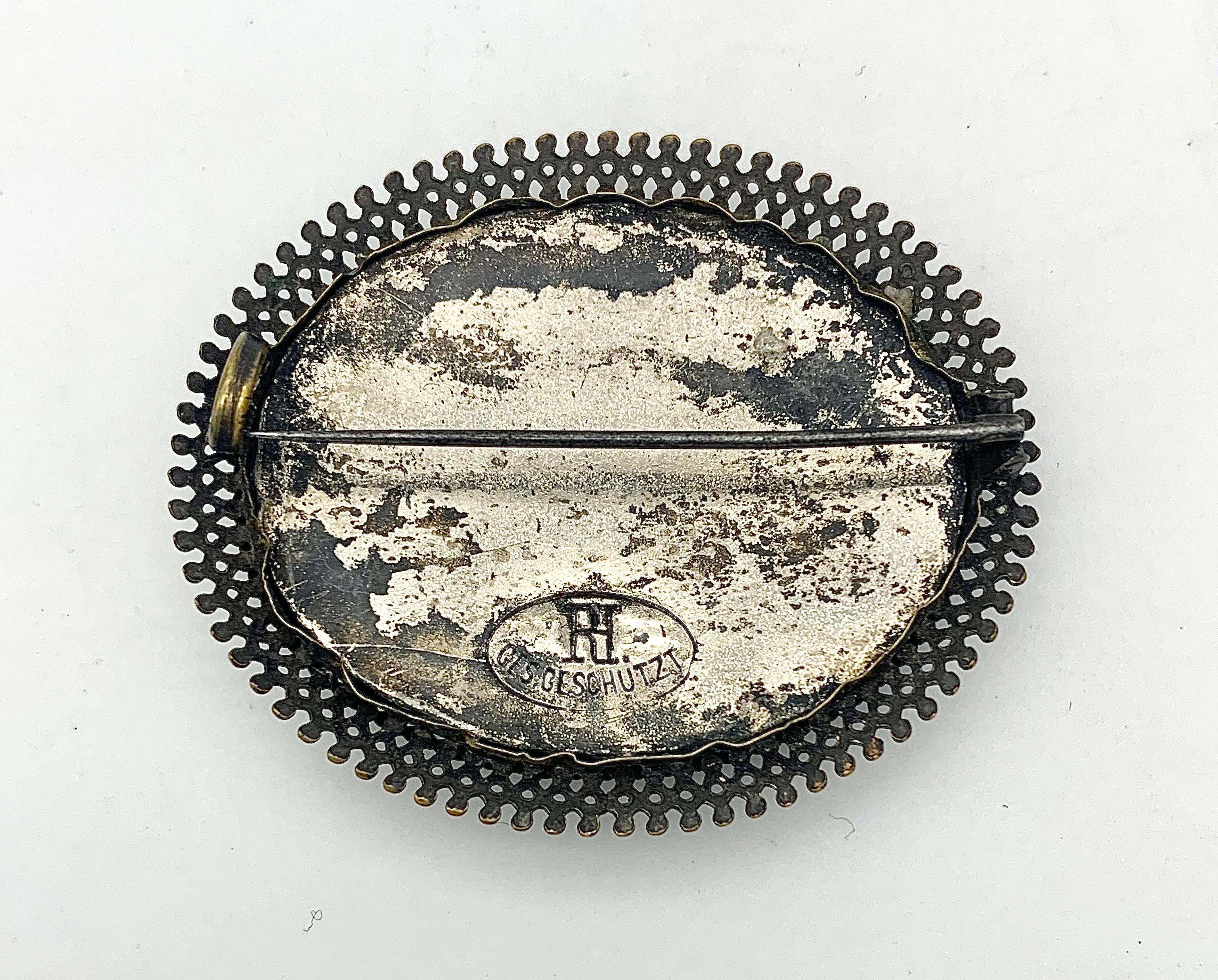 This unusual brooch features a miniature diorama hand carved out of cork. The oval diorama shows a fortress surrounded by trees under a pale blue sky.. The cork carving is lined with painted paper and mounted in a mixed metall frame. The brooch has