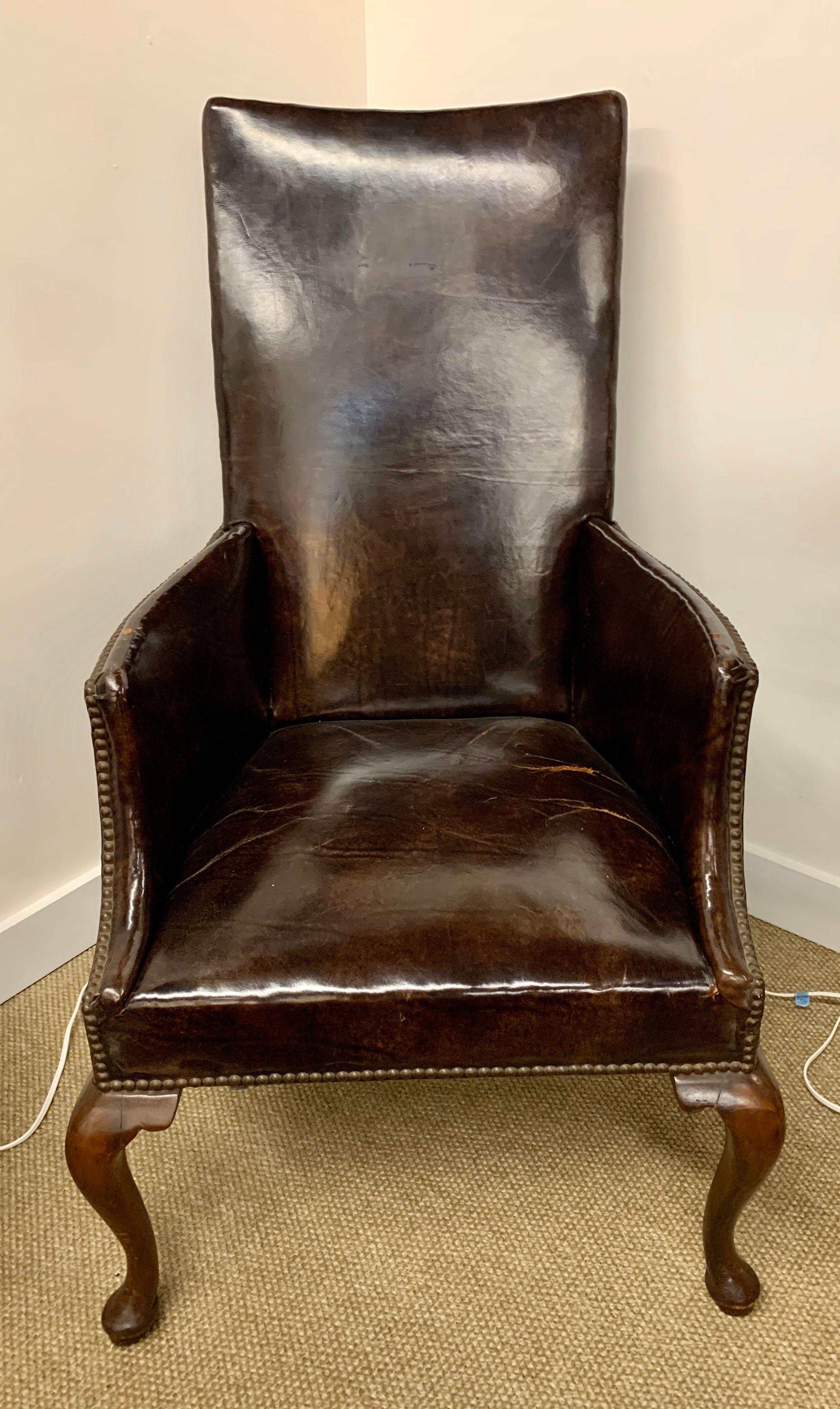 Elegant antique brown leather reading chair adorned with brass nailheads and mahogany base, all original. The patina on the leather is broken in just perfect. This piece is guaranteed to make an immediate statement in any room. All dimensions are